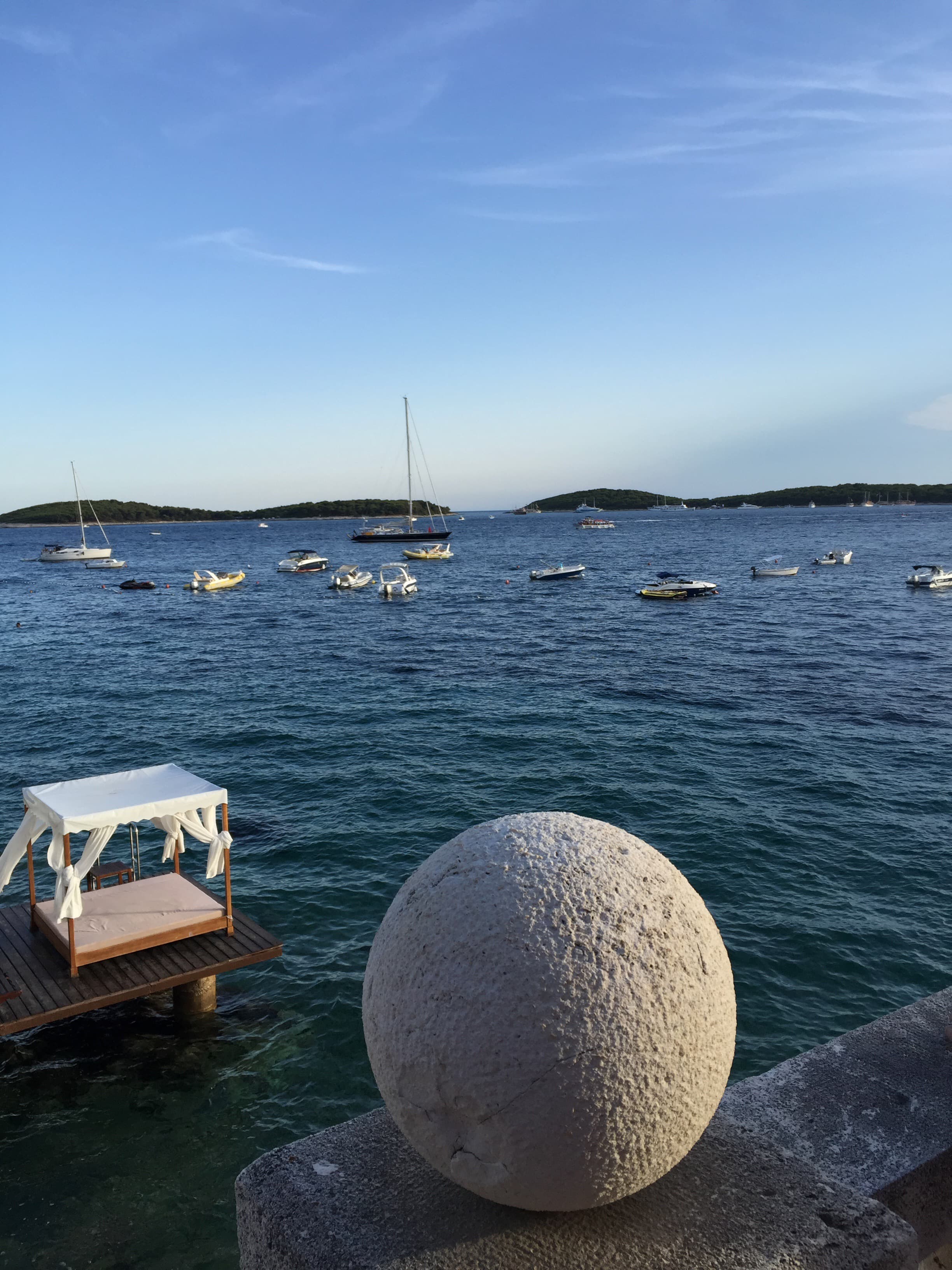 Boats sail to the horizon as waves lap the shore on a sunny day.