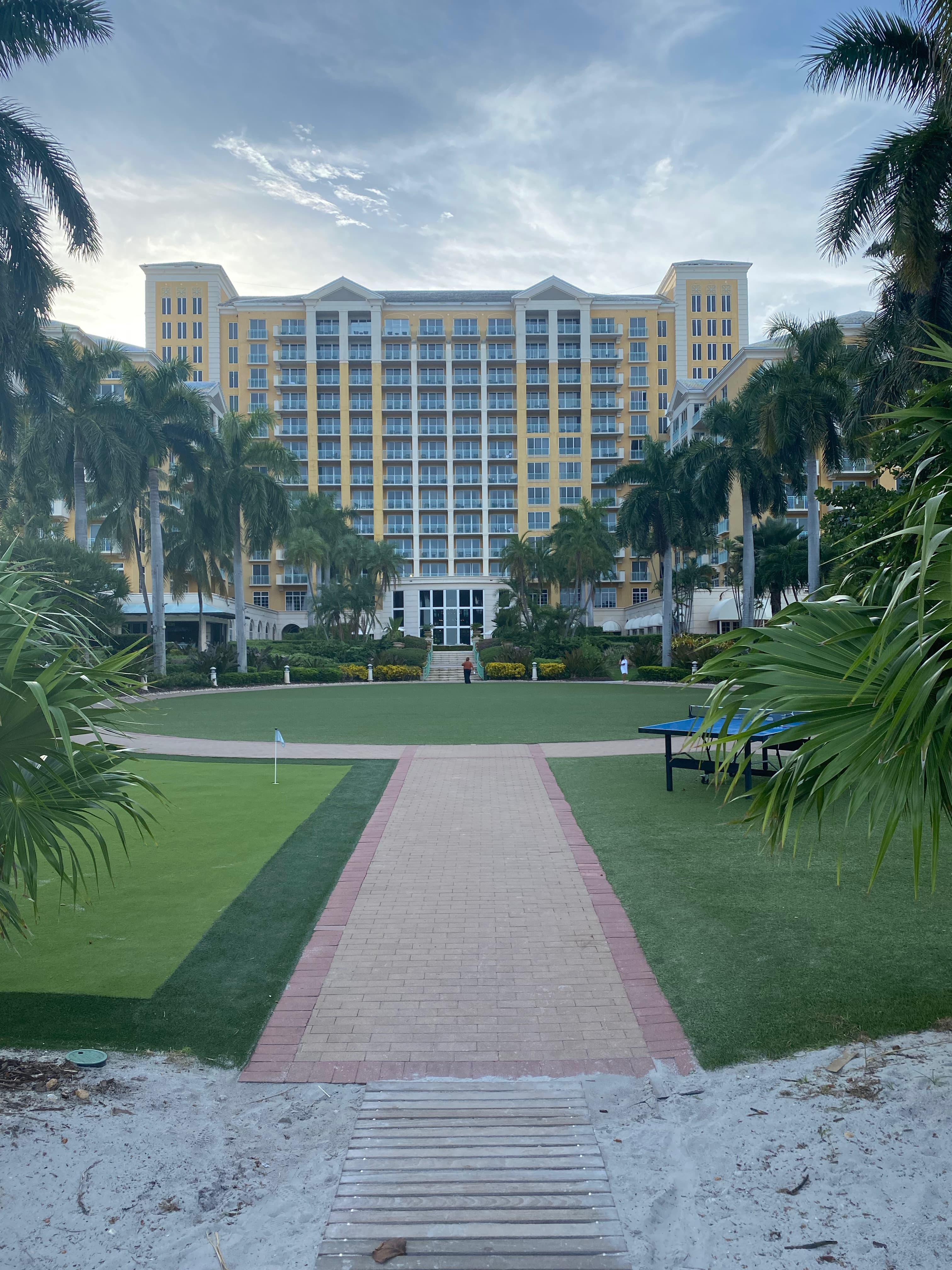 A hotel frames the hazy sky as a grassy plaza and palm trees line the foreground.