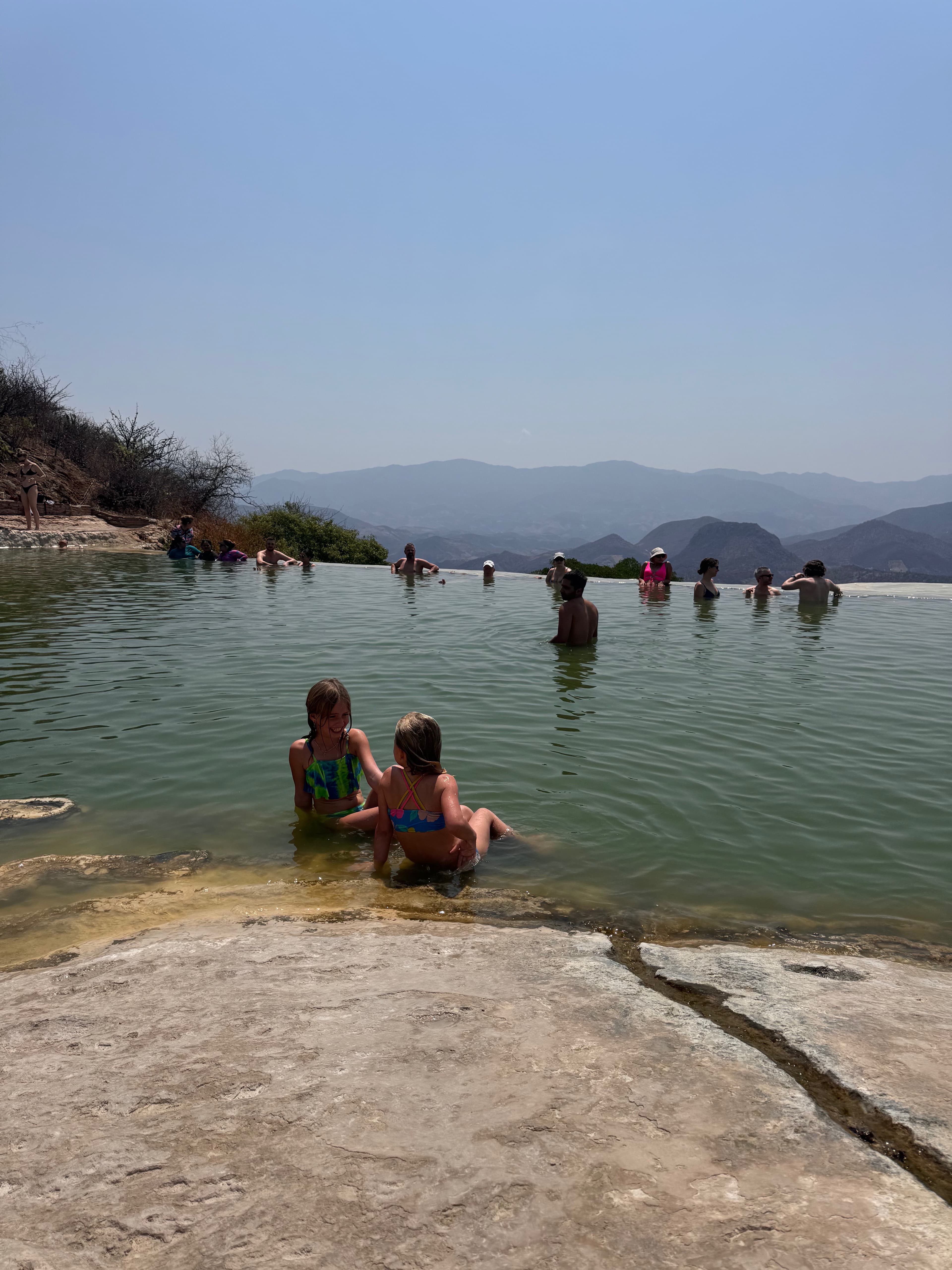 View of two children sitting in shallow water with a mountain range in the distance on a sunny day
