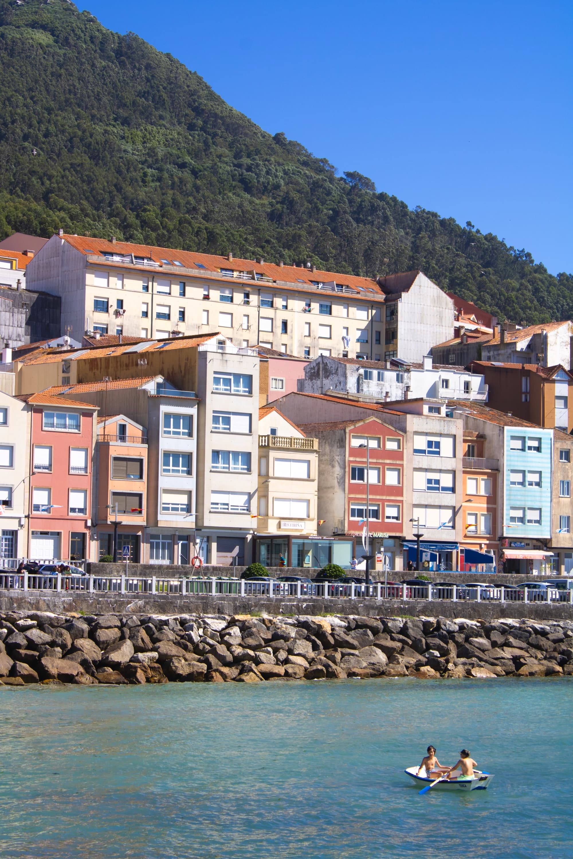 A serene body of water reflecting the sky, surrounded by lush greenery and distant hills and the city in the background.