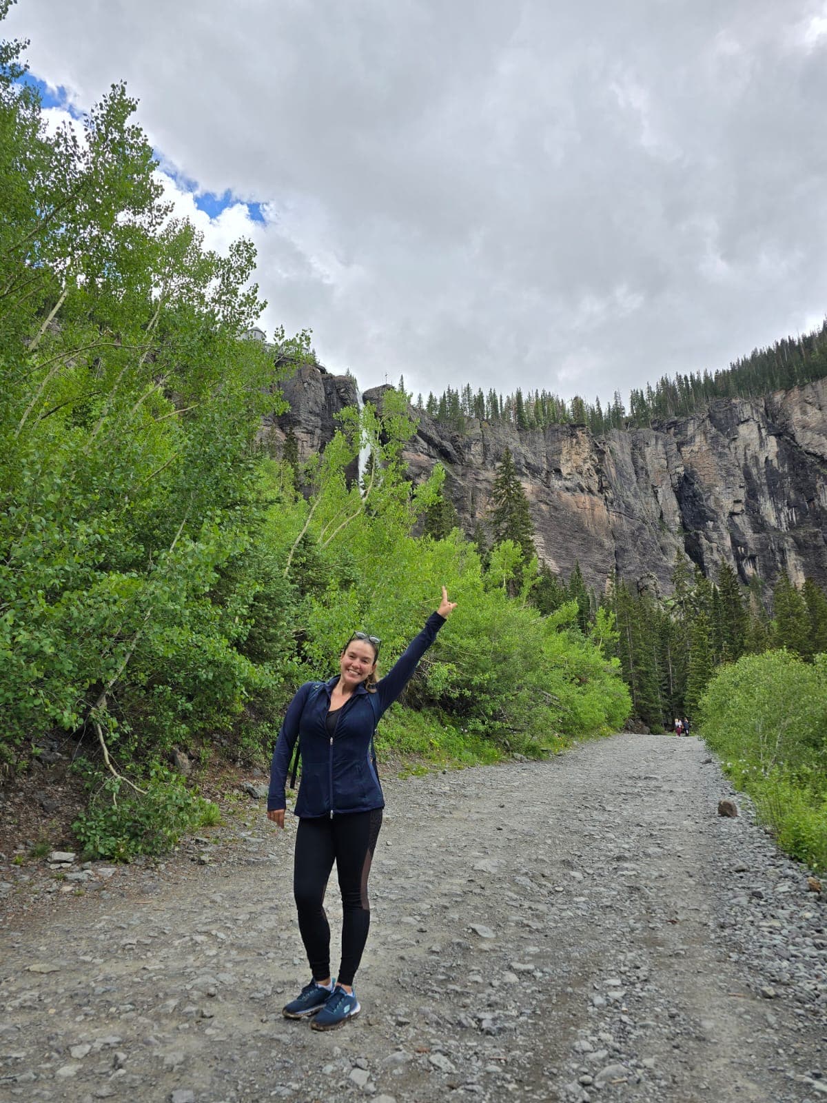 Advisor in all black exercise clothing on a gravel road with cliffs and trees in the background