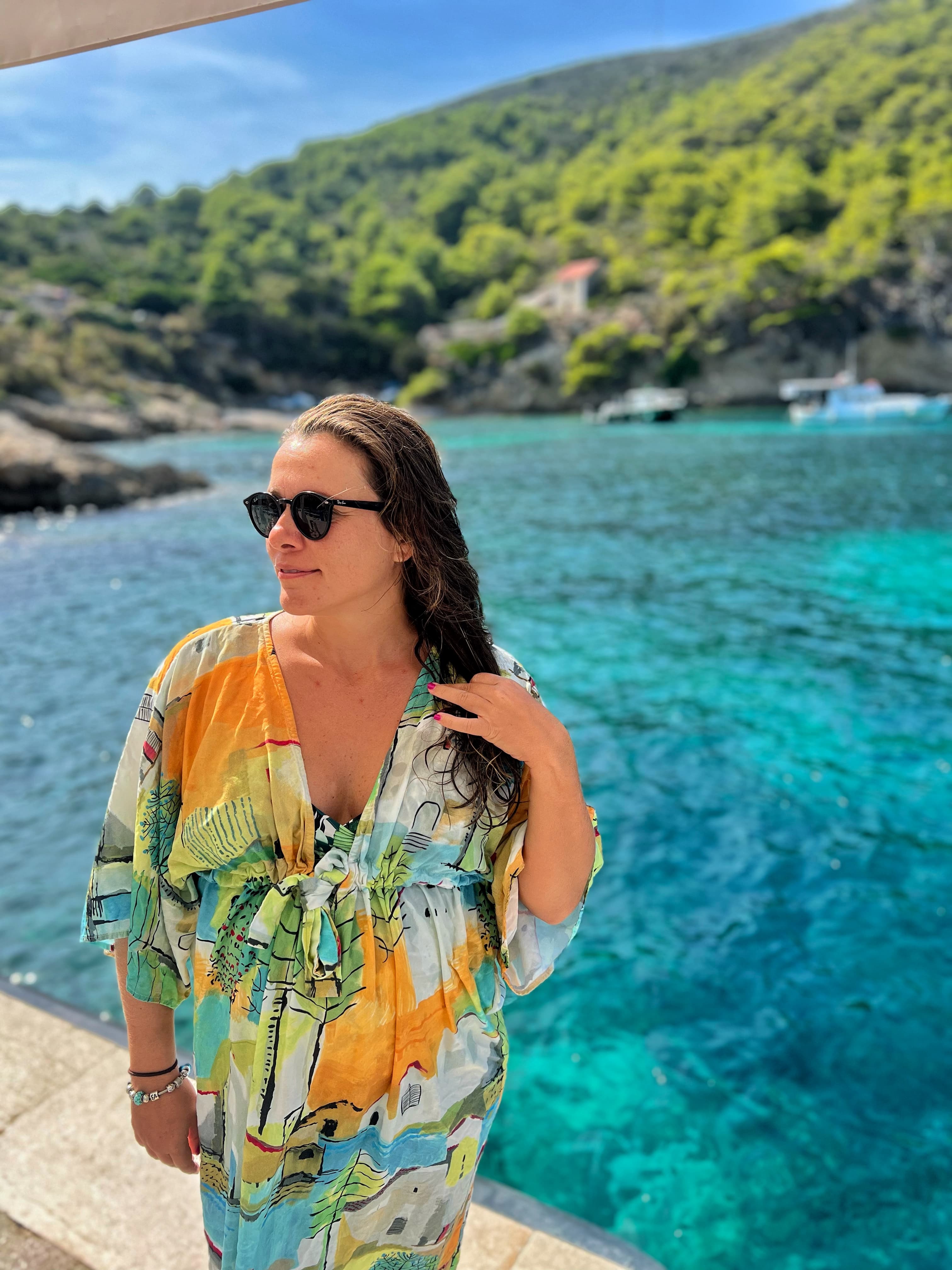 Advisor in a dress and black sunglasses with a beautiful ocean and leafy coastline in the background