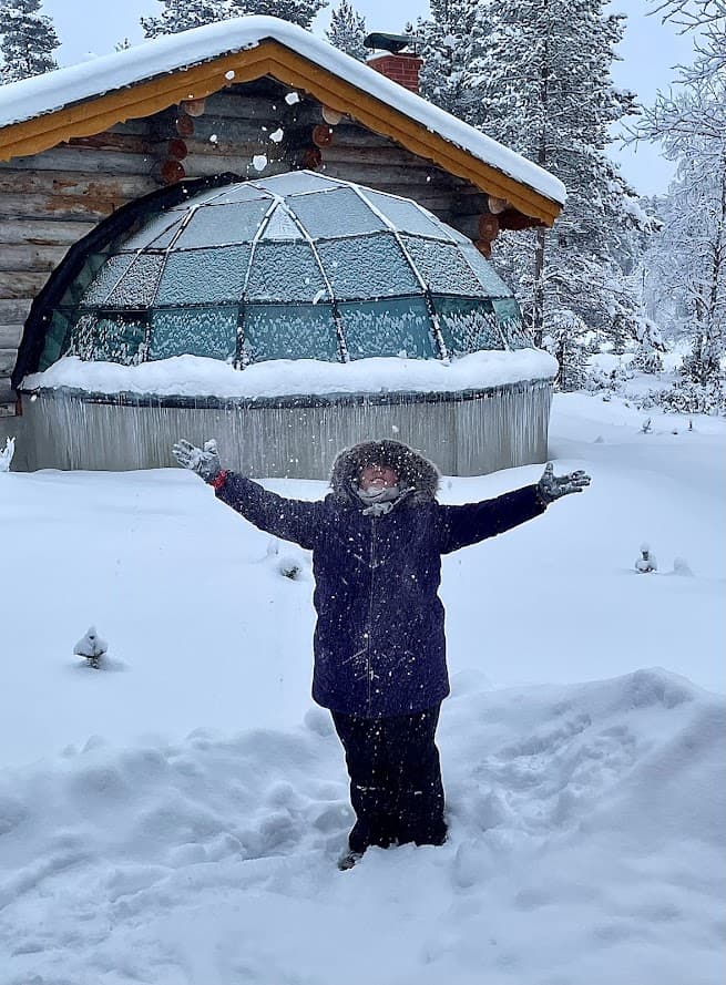 Kate joyfully extends her arms in the snow, surrounded by a serene winter scene.