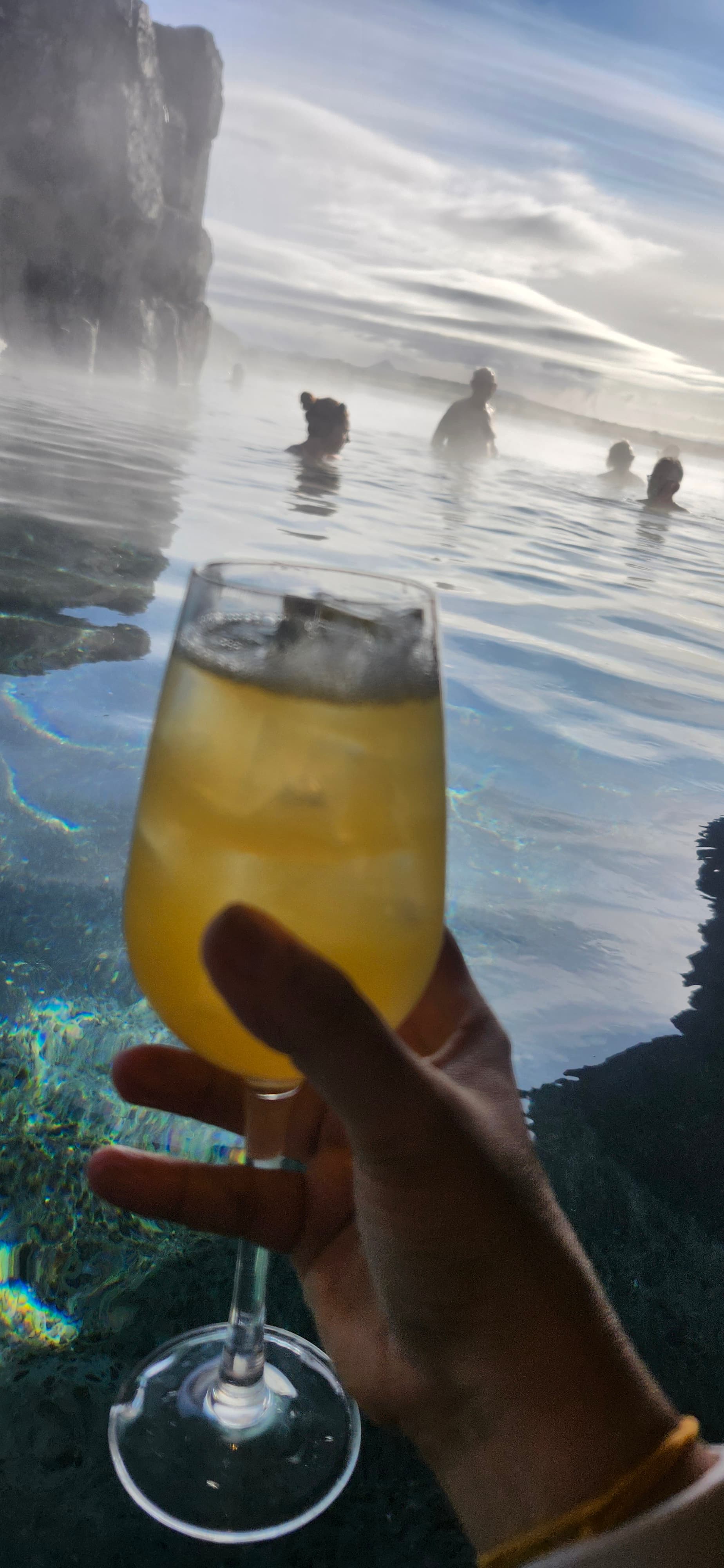 Hand holding a cocktail beside a pool during the day