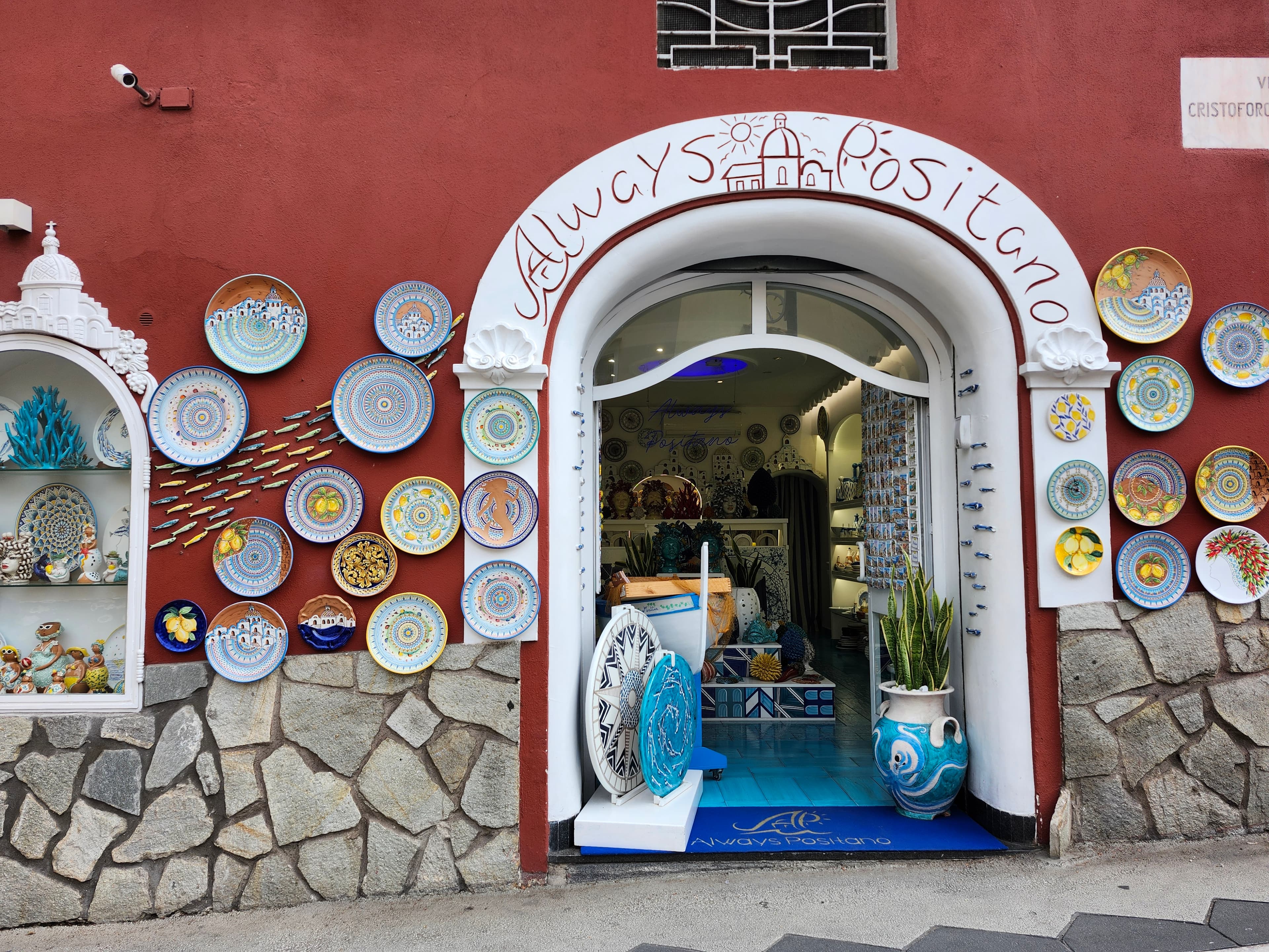View of a storefront with plates hanging on the red wall in Positano