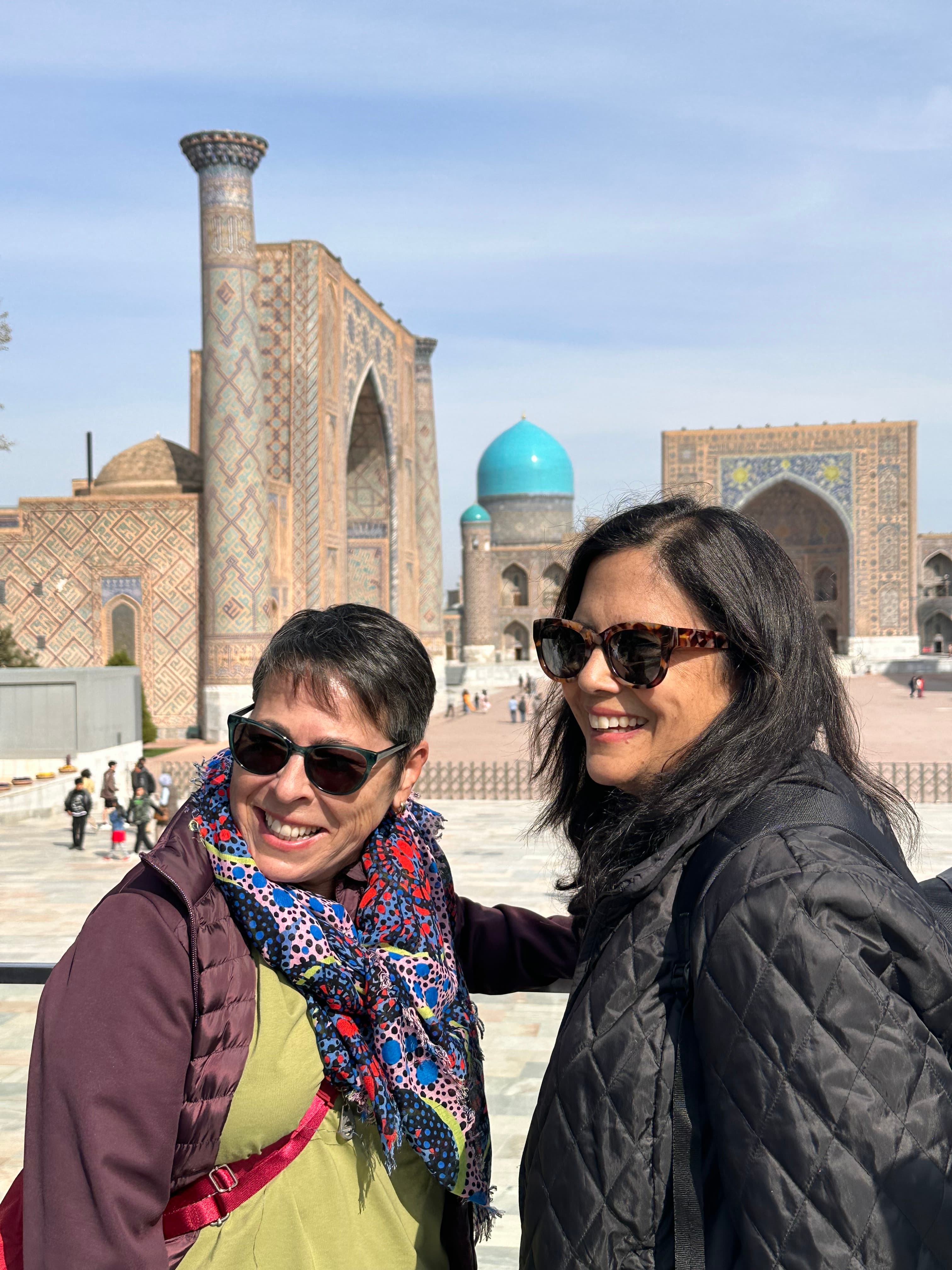 Advisor and a friend smiling together outdoors on a sunny day with a blue-domed mosque visible in the distance