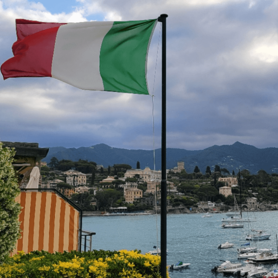 View of the red, white and green Italian flag flying over a seaside town on a cloudy day