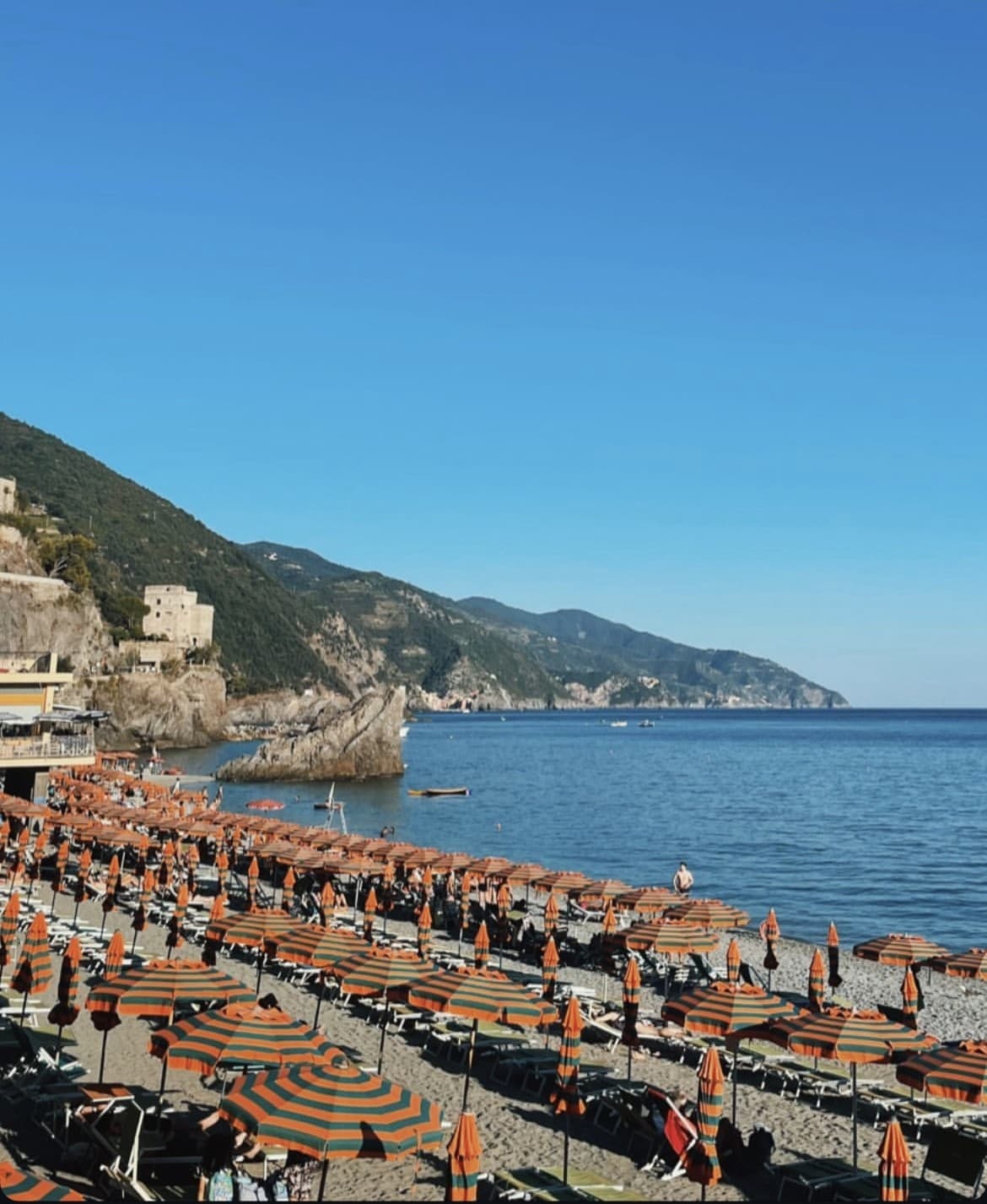 View of orange striped umbrellas in rows on a rocky beach under clear skies