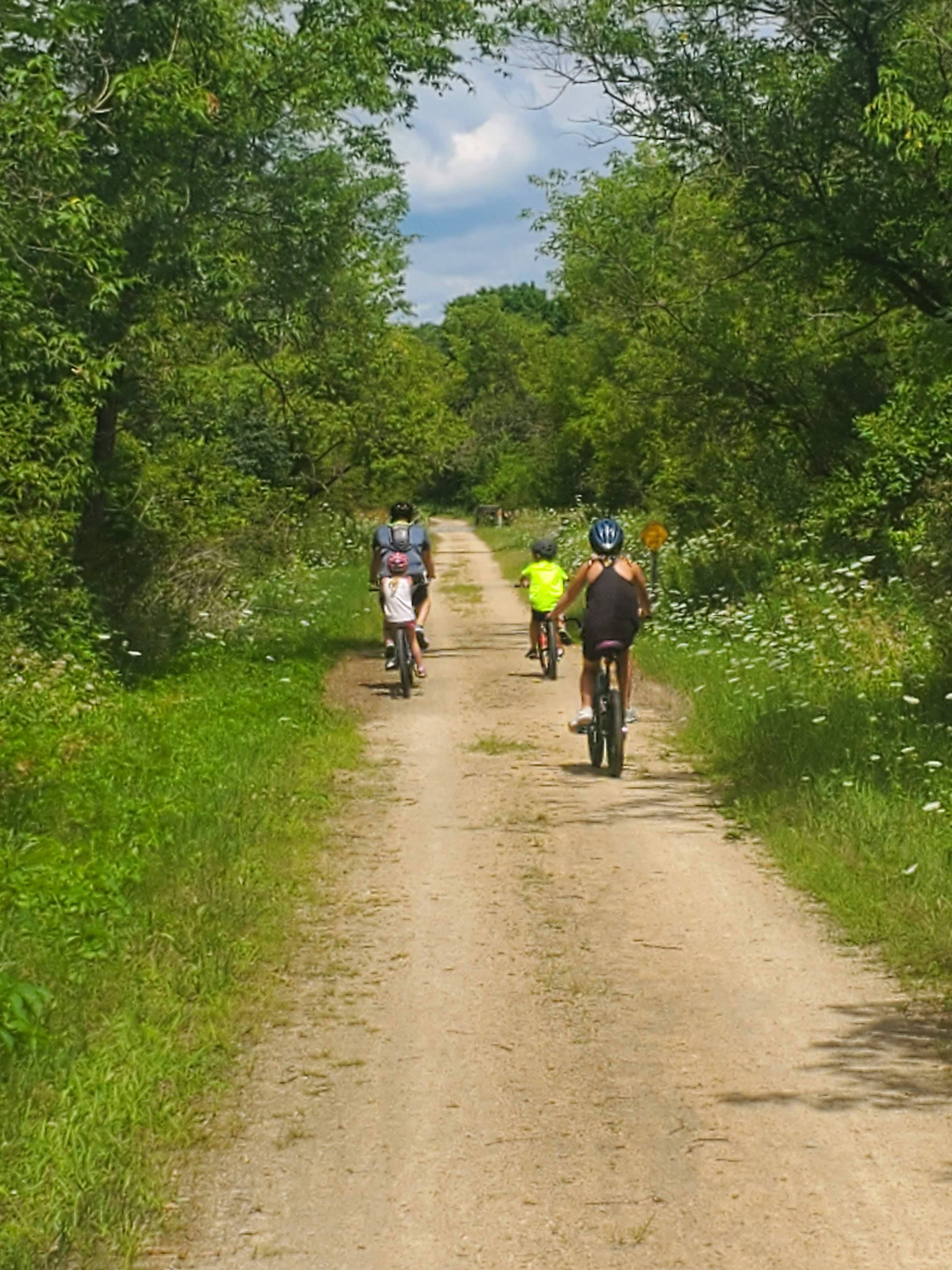 Advisor’s family riding bikes along a dirt path lined with leafy trees