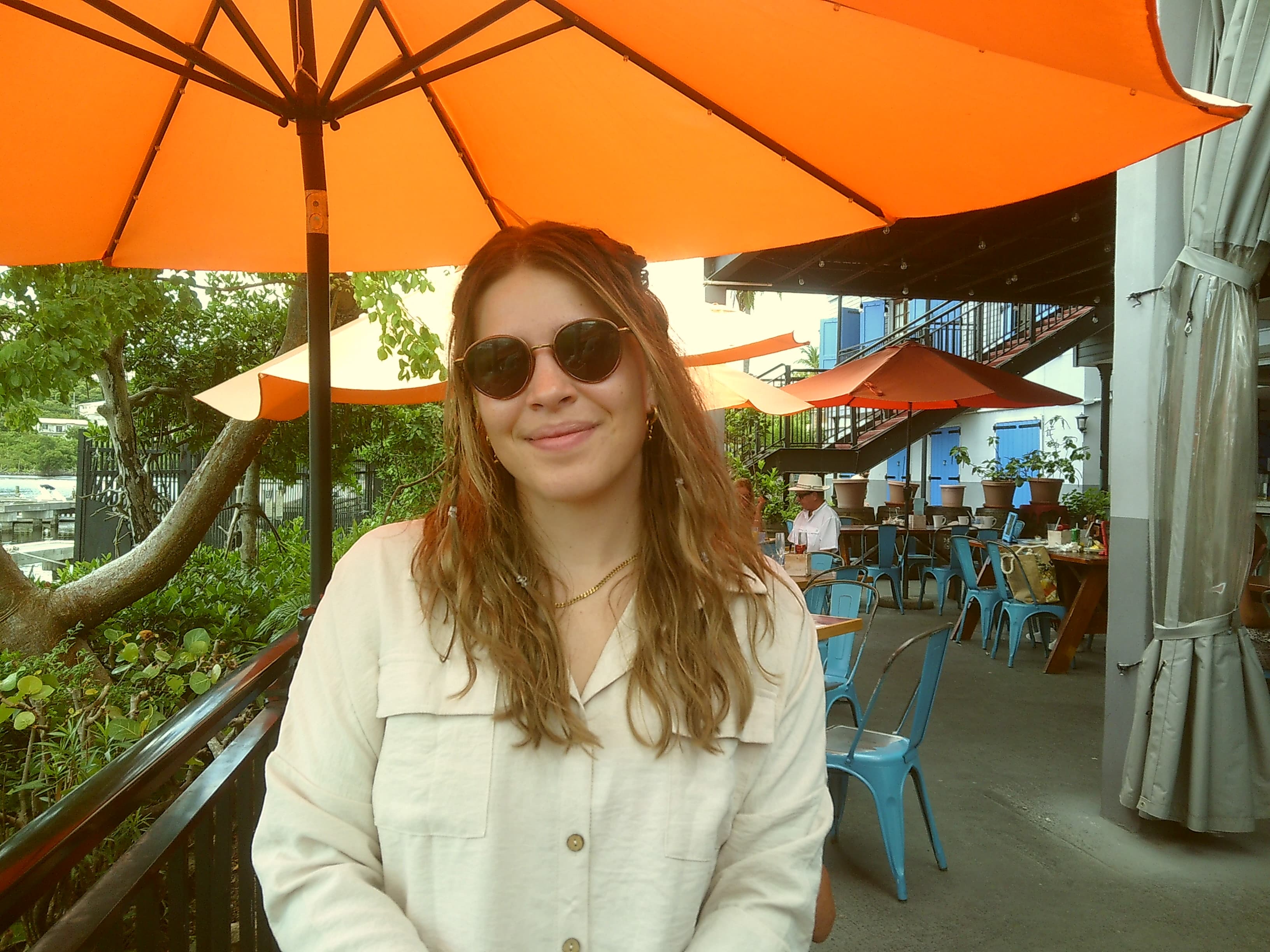 Advisor in a white button down shirt and sunglasses sitting outdoors under an orange umbrella