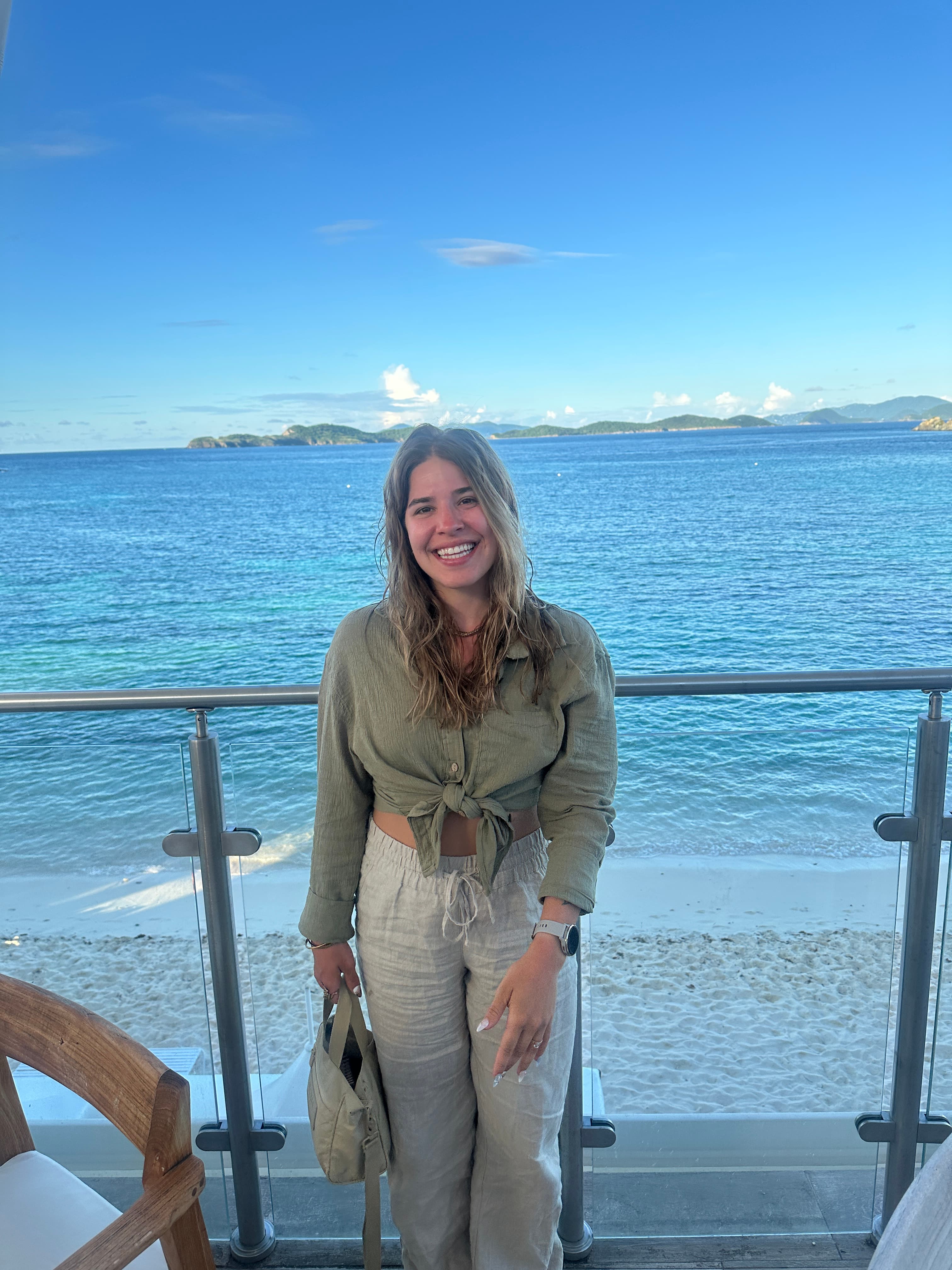 Advisor in beige trousers and a green shirt smiling by the sea on a sunny day