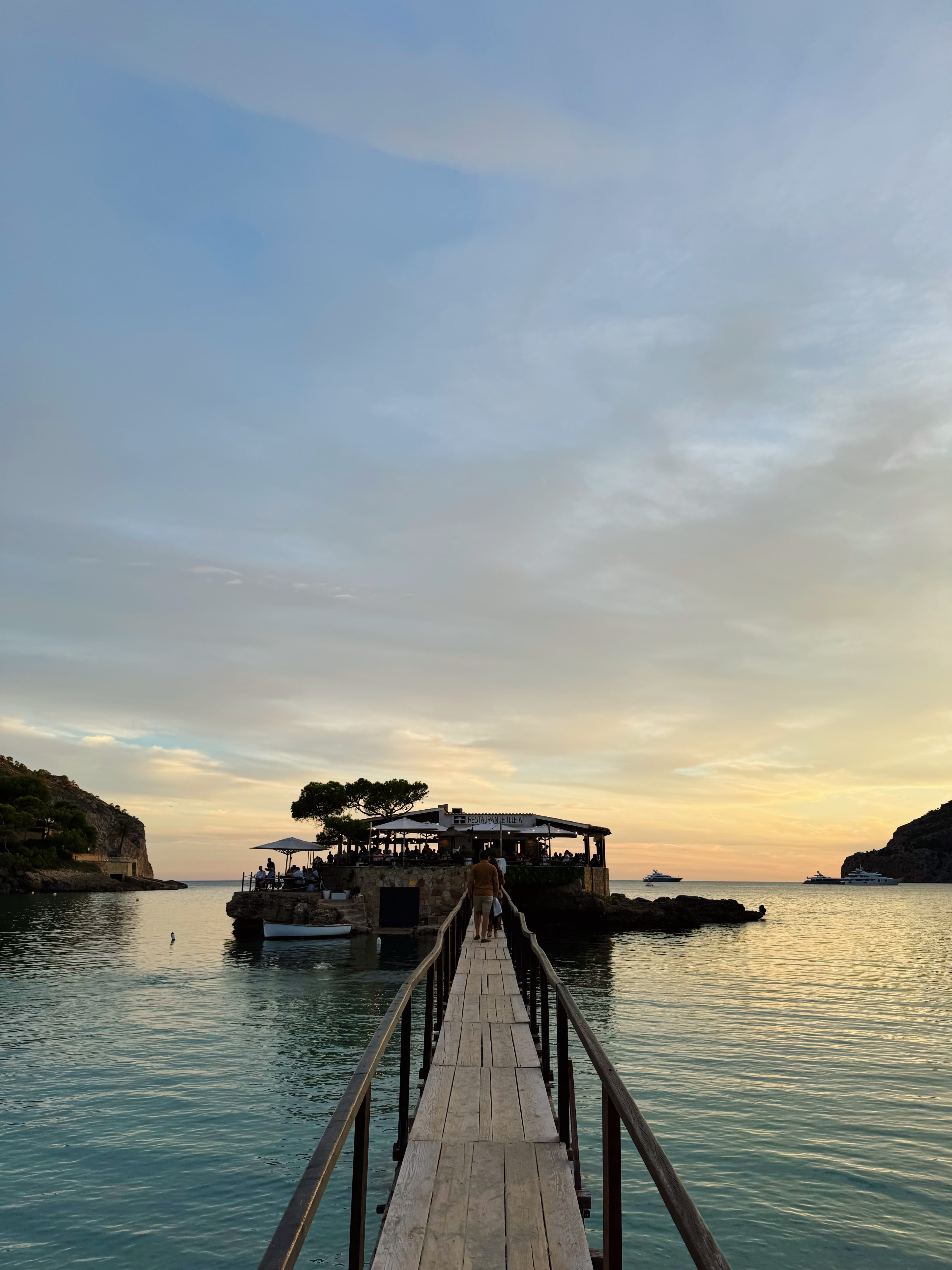 View of a narrow wooden pier with a boat docked at the end at sunset