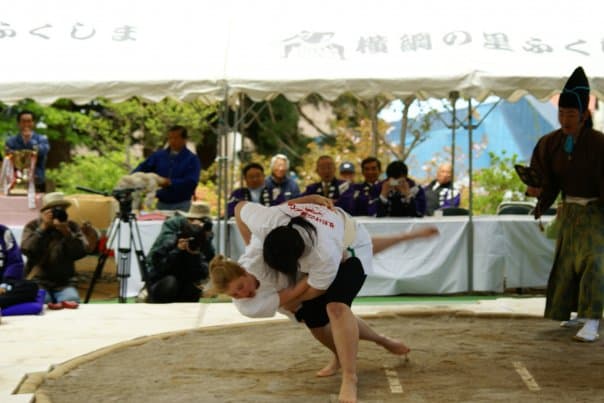A wrestling event with two people in T-shirts and shorts in an outdoor ring.