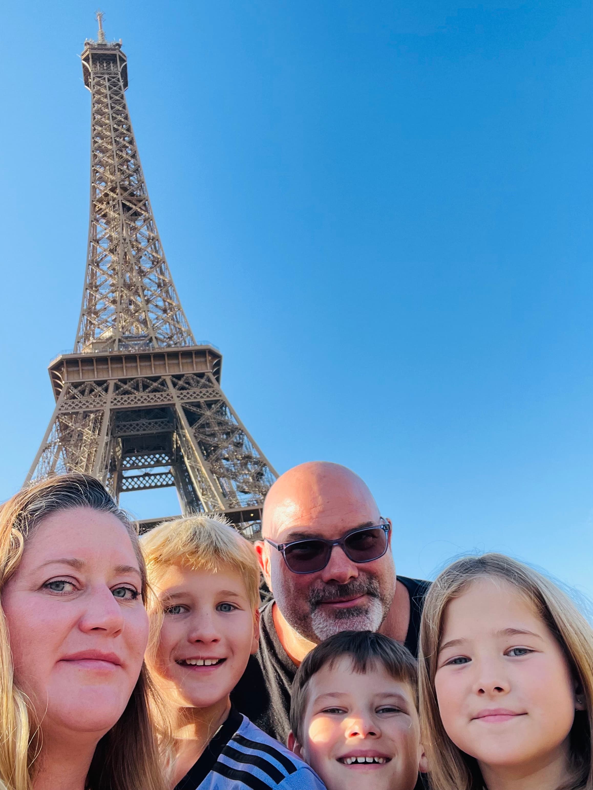 Karyn and her family posing in front of the Eiffel tower with clear skies in the distance.