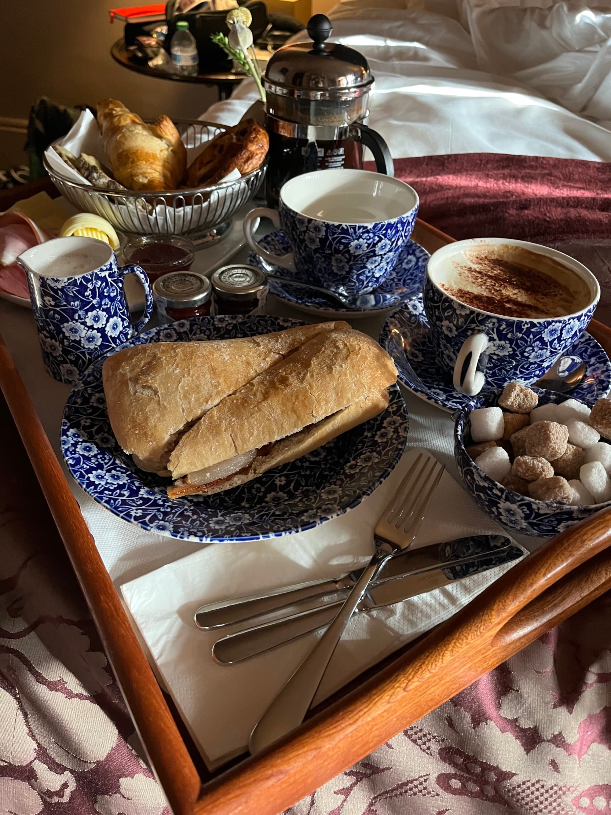 bread, coffee in blue mugs, and sugar cubes on a tray in bed