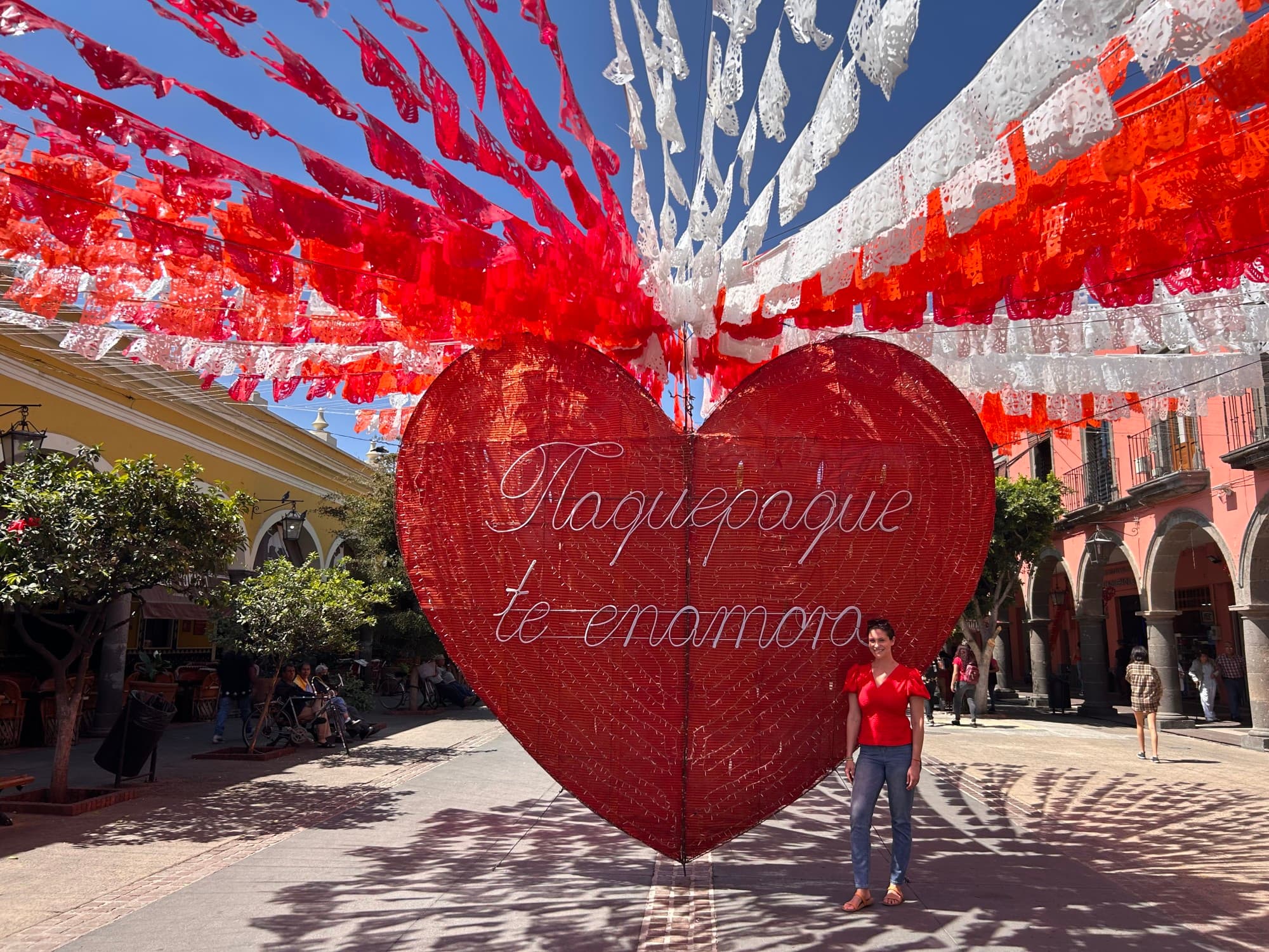 A woman stands in front of a large sculpture of a red heart.