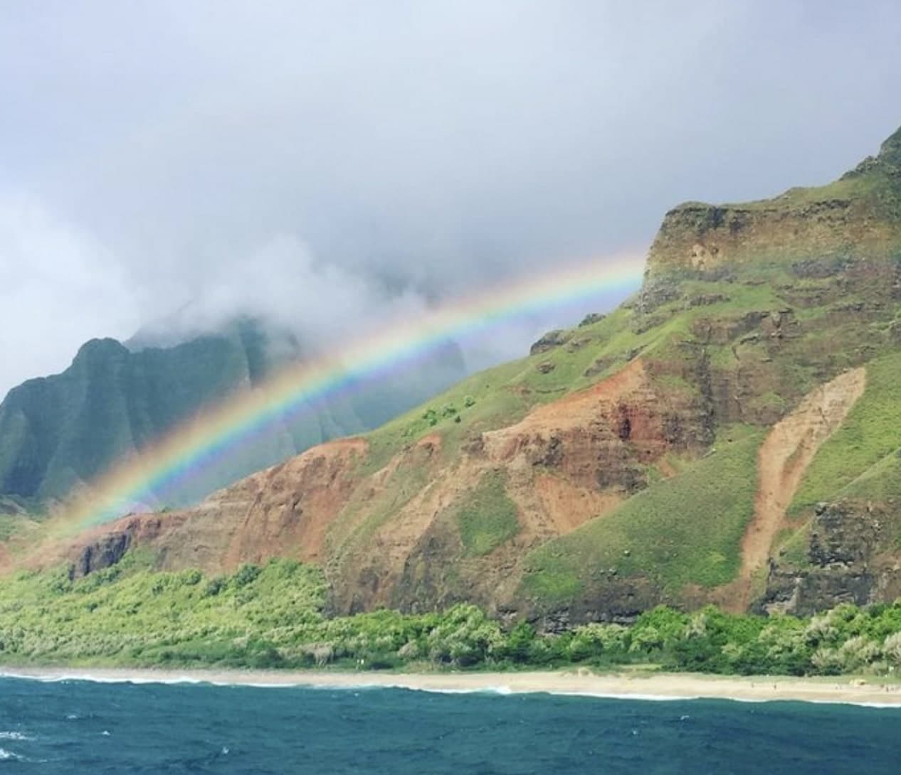 Picture of rainbow over lake at Nā Pali Coast State Wilderness Park with a shoreline and foliage.