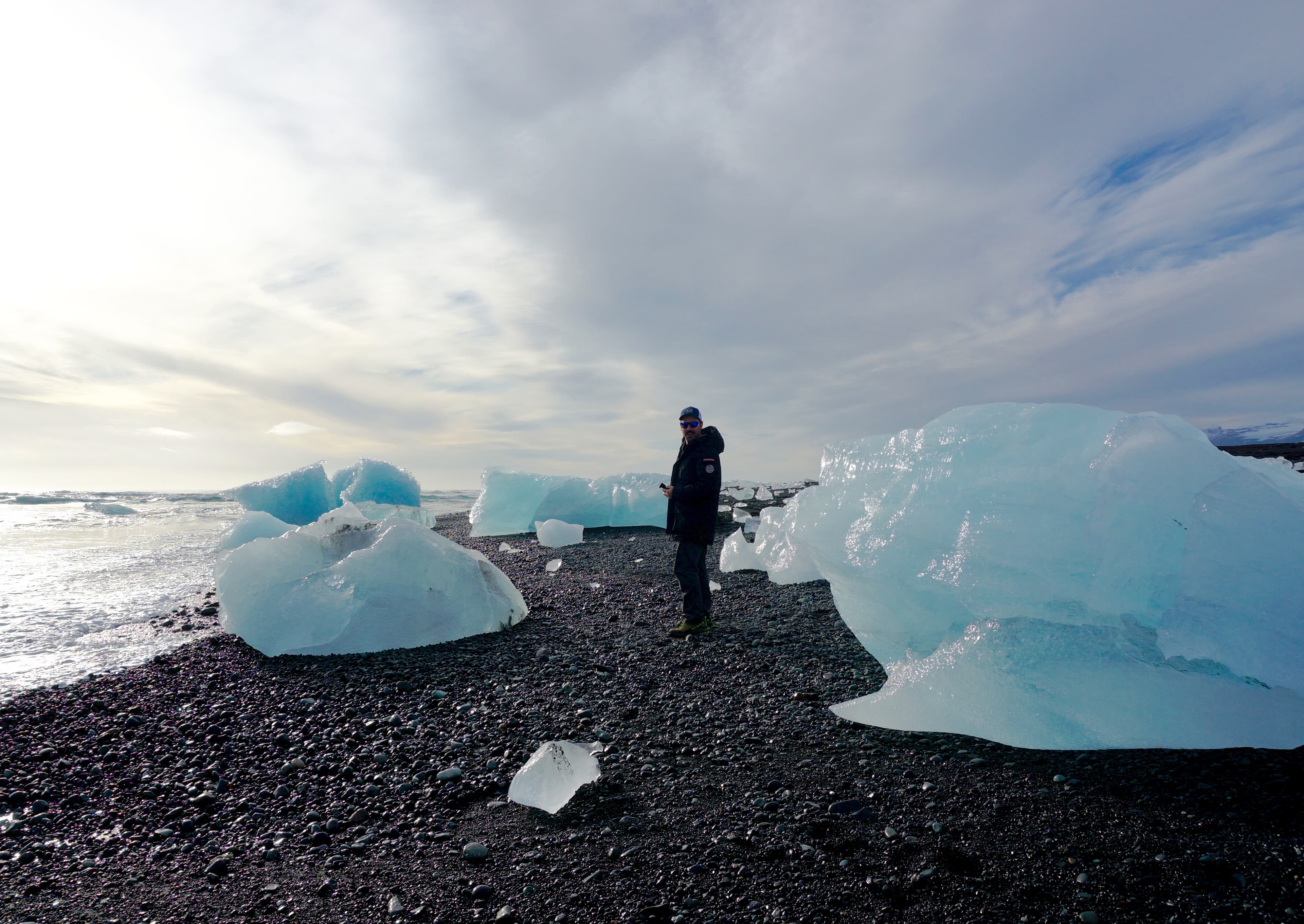 Kara standing on a rocky shore with large ice bergs around her and a shoreline to the left