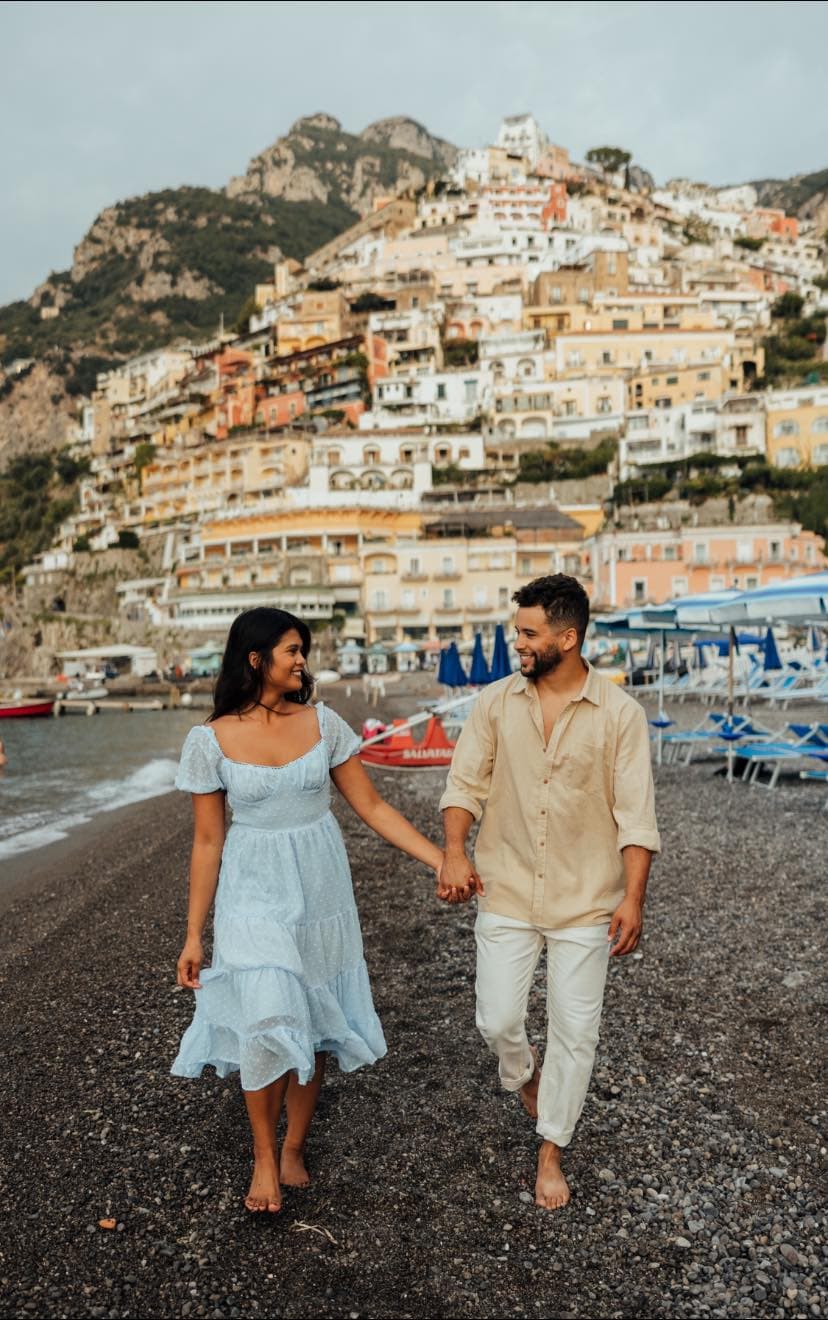A man and woman walking on a beach holding hands.