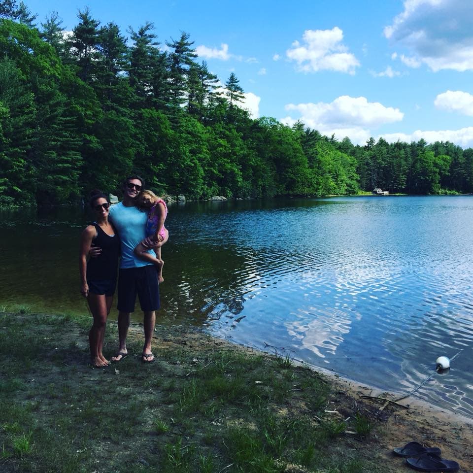 Amber posing with family in front of a lake surrounded by green trees.