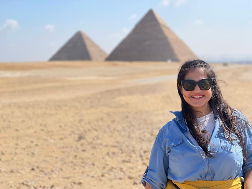 Mariela wearing a blue top and sunglasses standing in front of the Great Pyramids of Giza