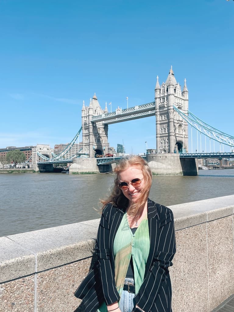 Picture of Merritt at Tower Bridge in London on a sunny day wearing a green top, black jacket and sunglasses