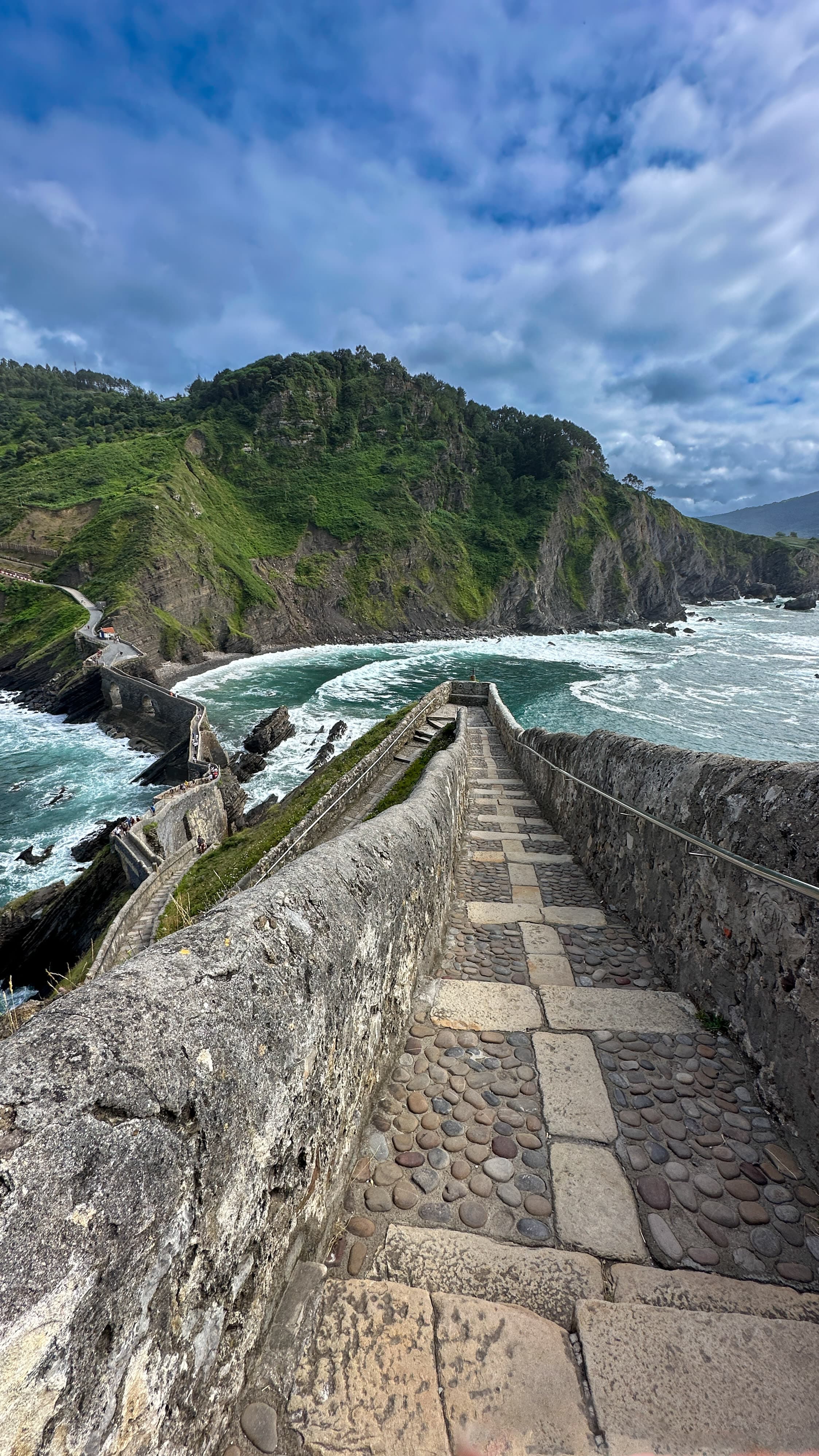 A stone pathway going downhill between Bermeo and Bakio with a mountain and water in the distance