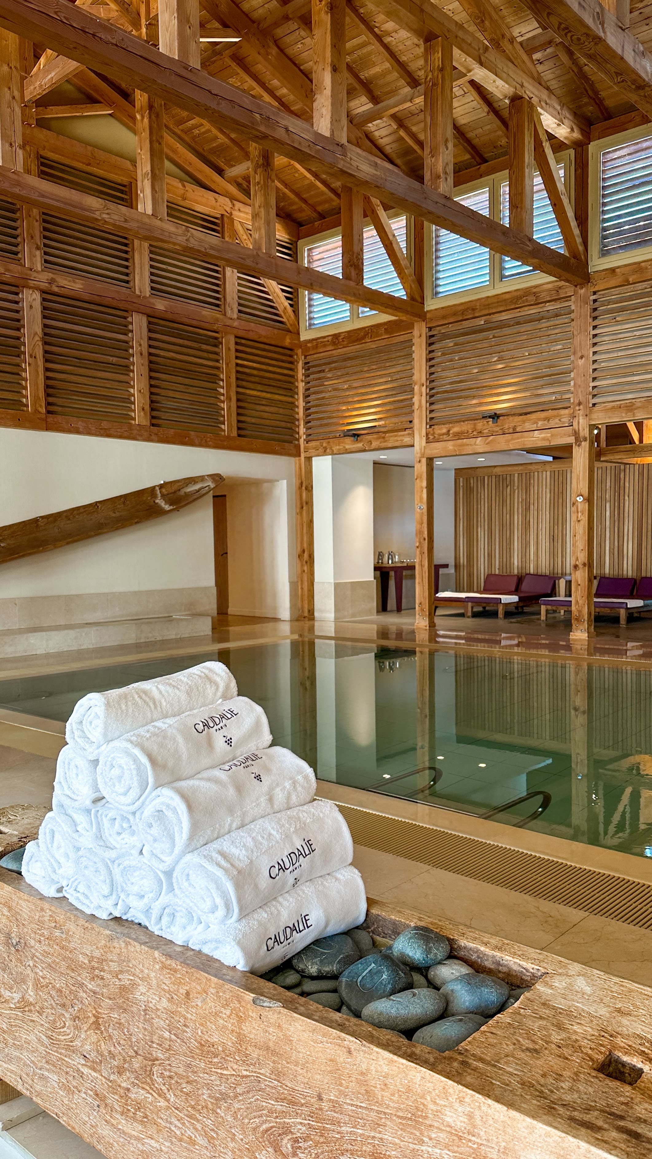 White towels rolled up near a swimming pool inside of a wooden building with ceiling beams