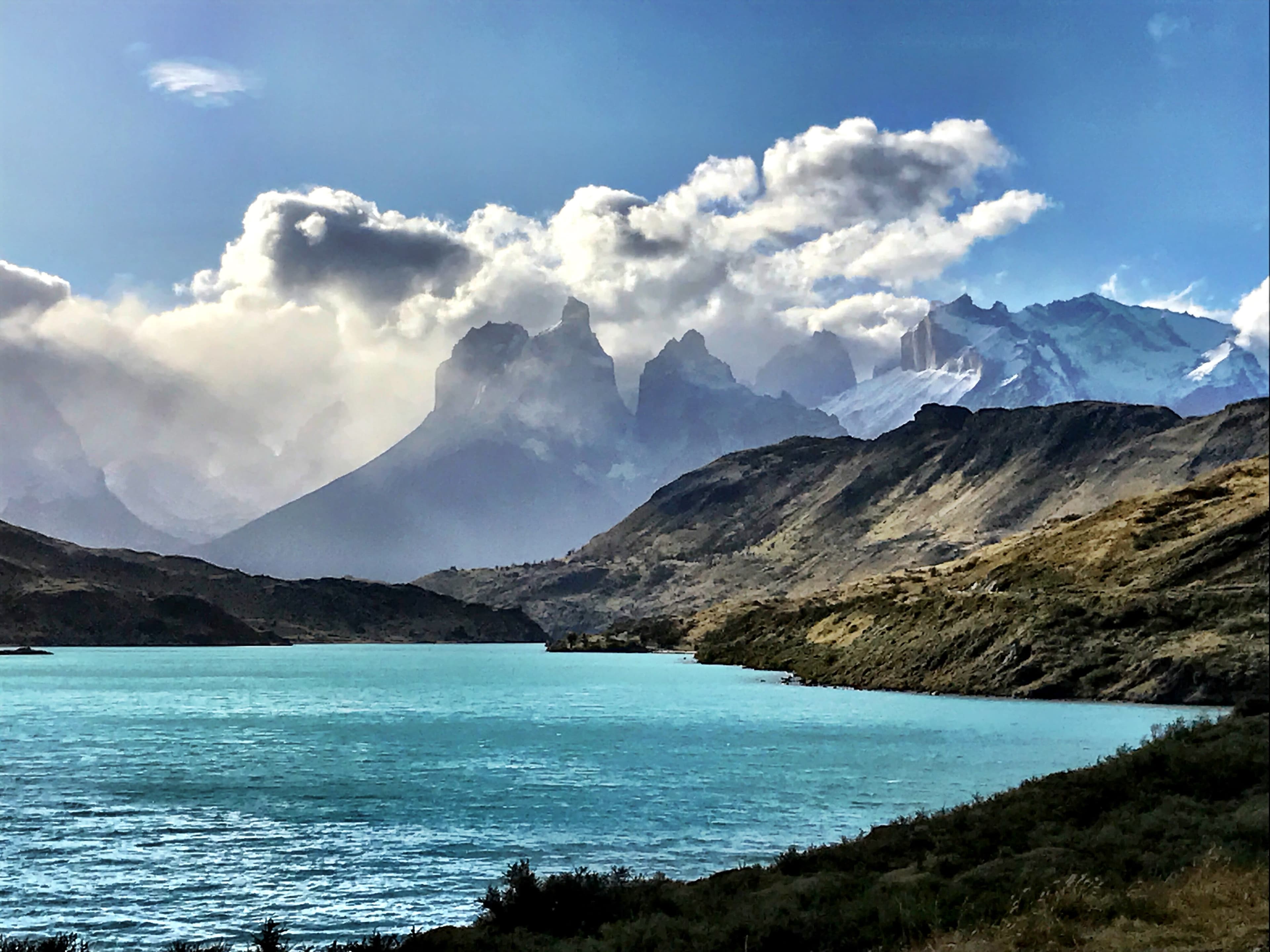 A turquoise lake next to tall rocky mountains on a sunny day with clouds