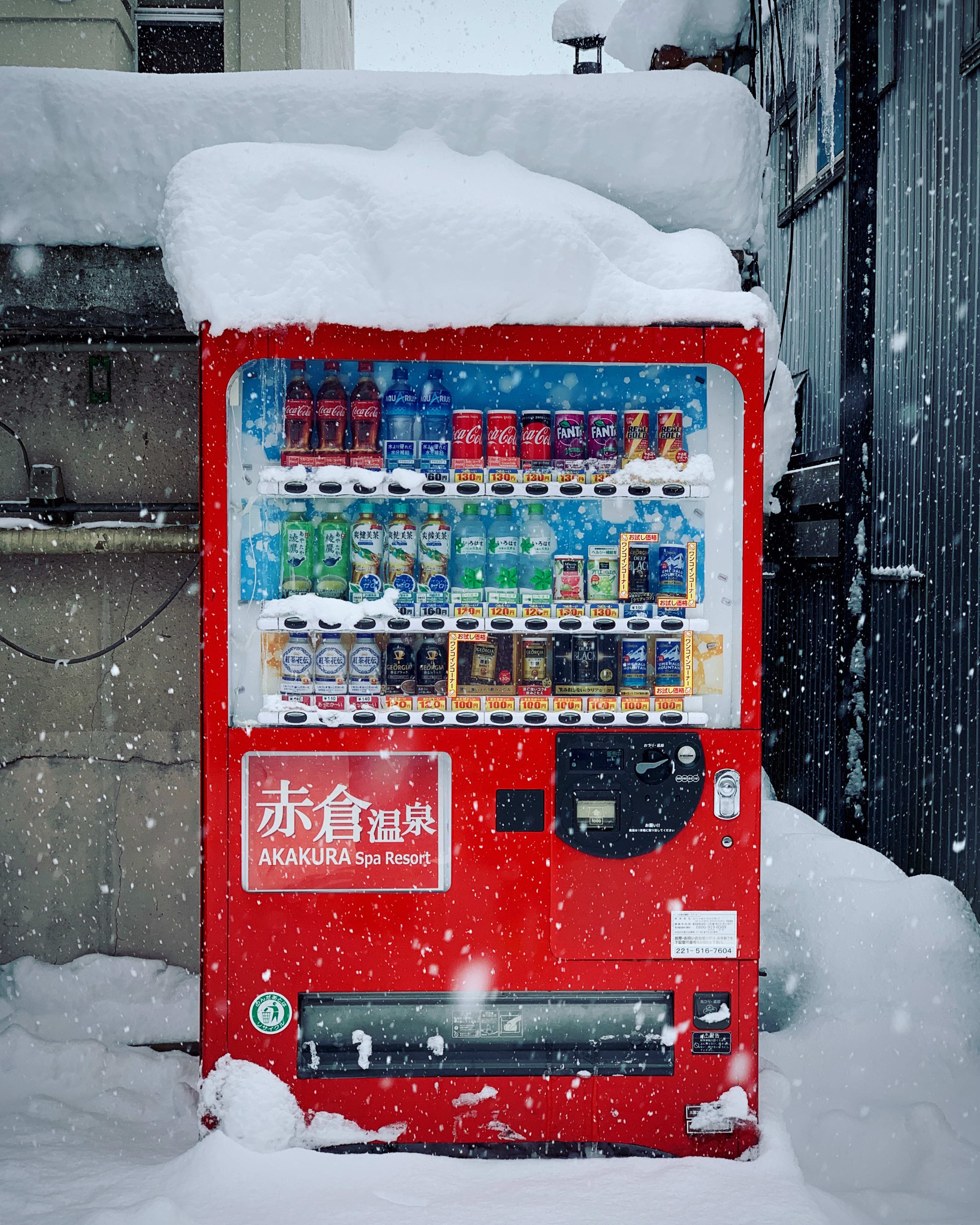 Red vending machine selling drinks covered in snow with a sign with Japanese letters