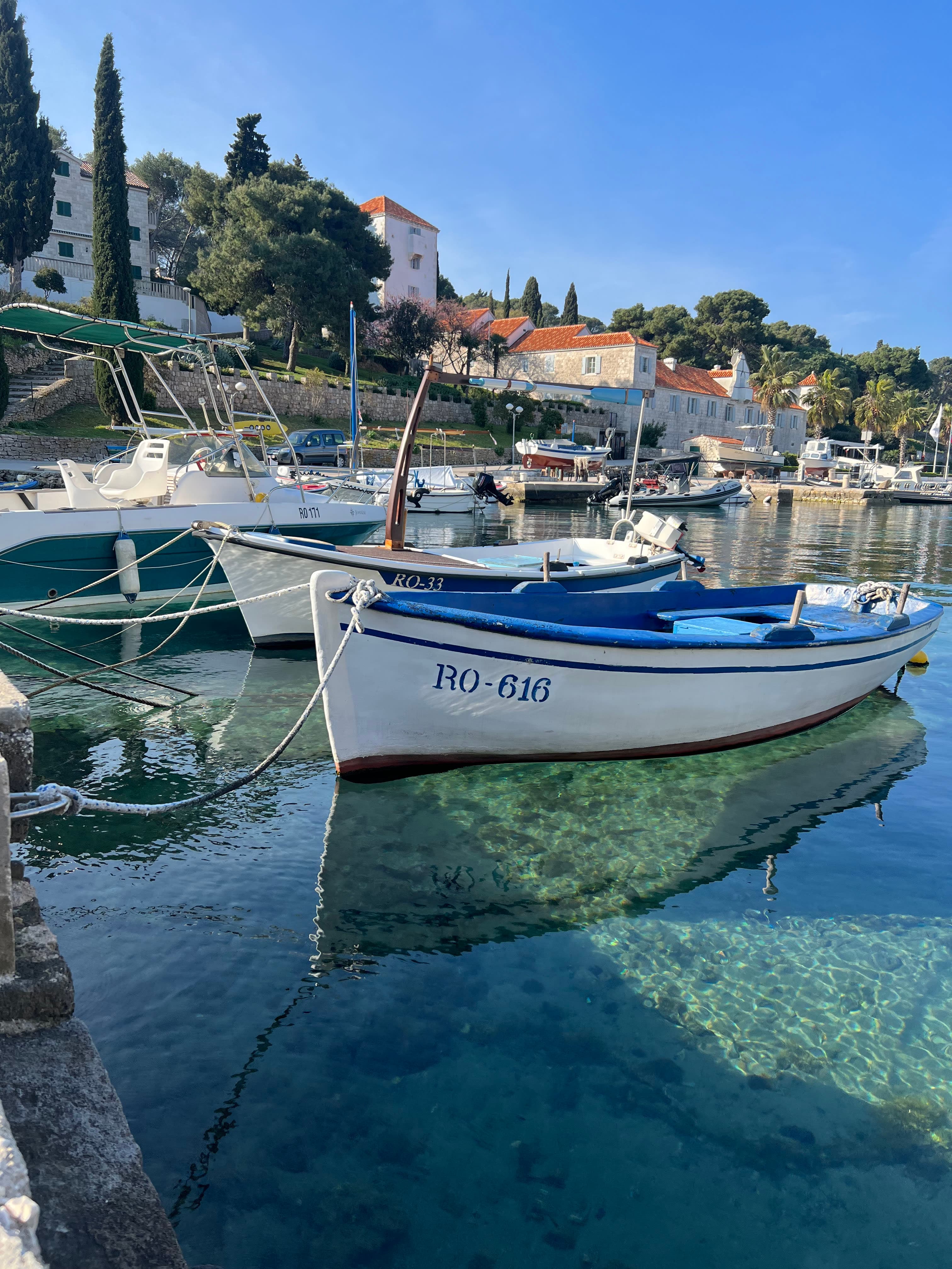 Smaller fisher boats tied up at a pier and floating on top of crystal clear, blue water.
