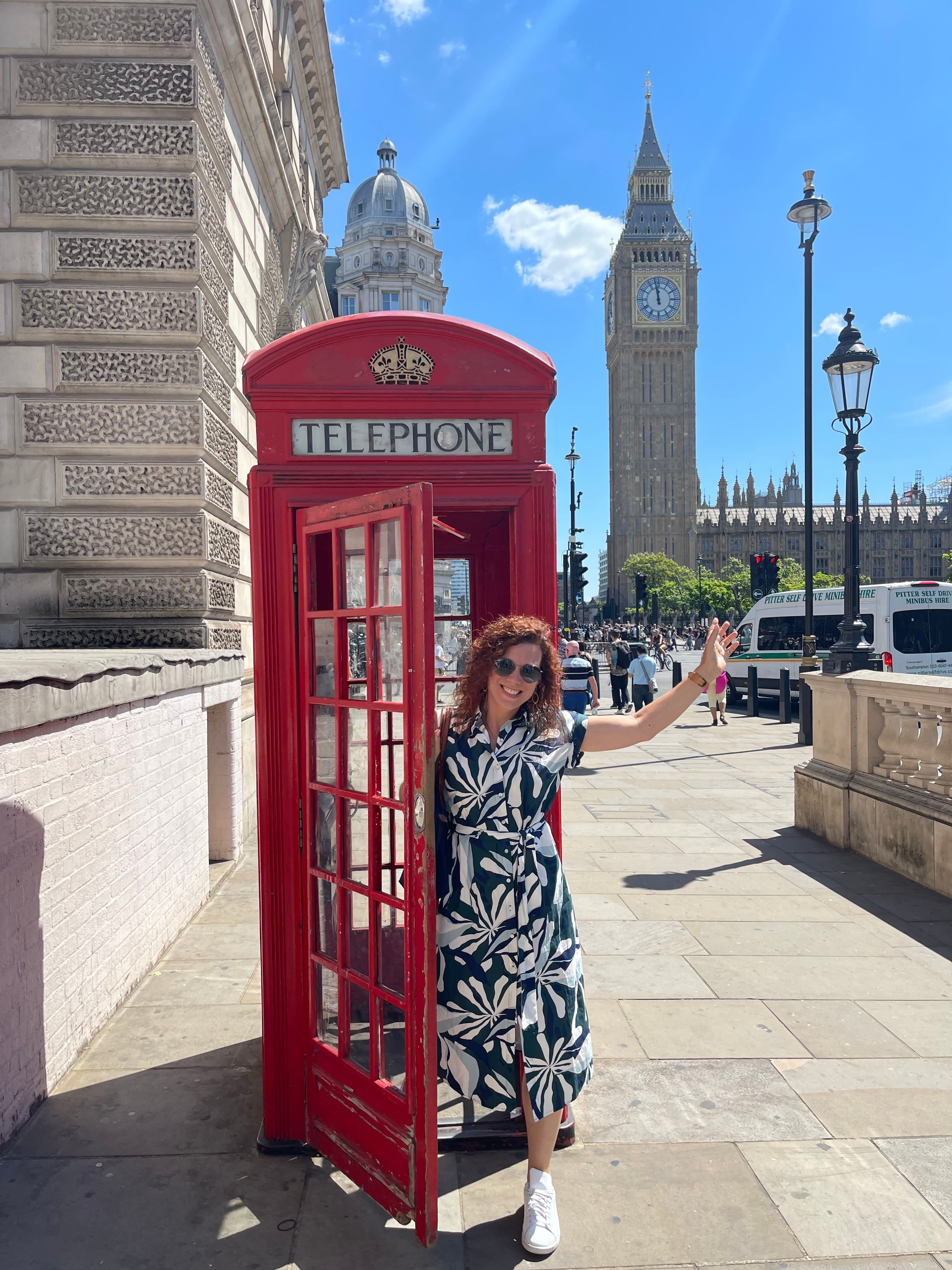 Travel advisor Alexandra coming out of a red phone booth in London with Big Ben in view on a sunny day