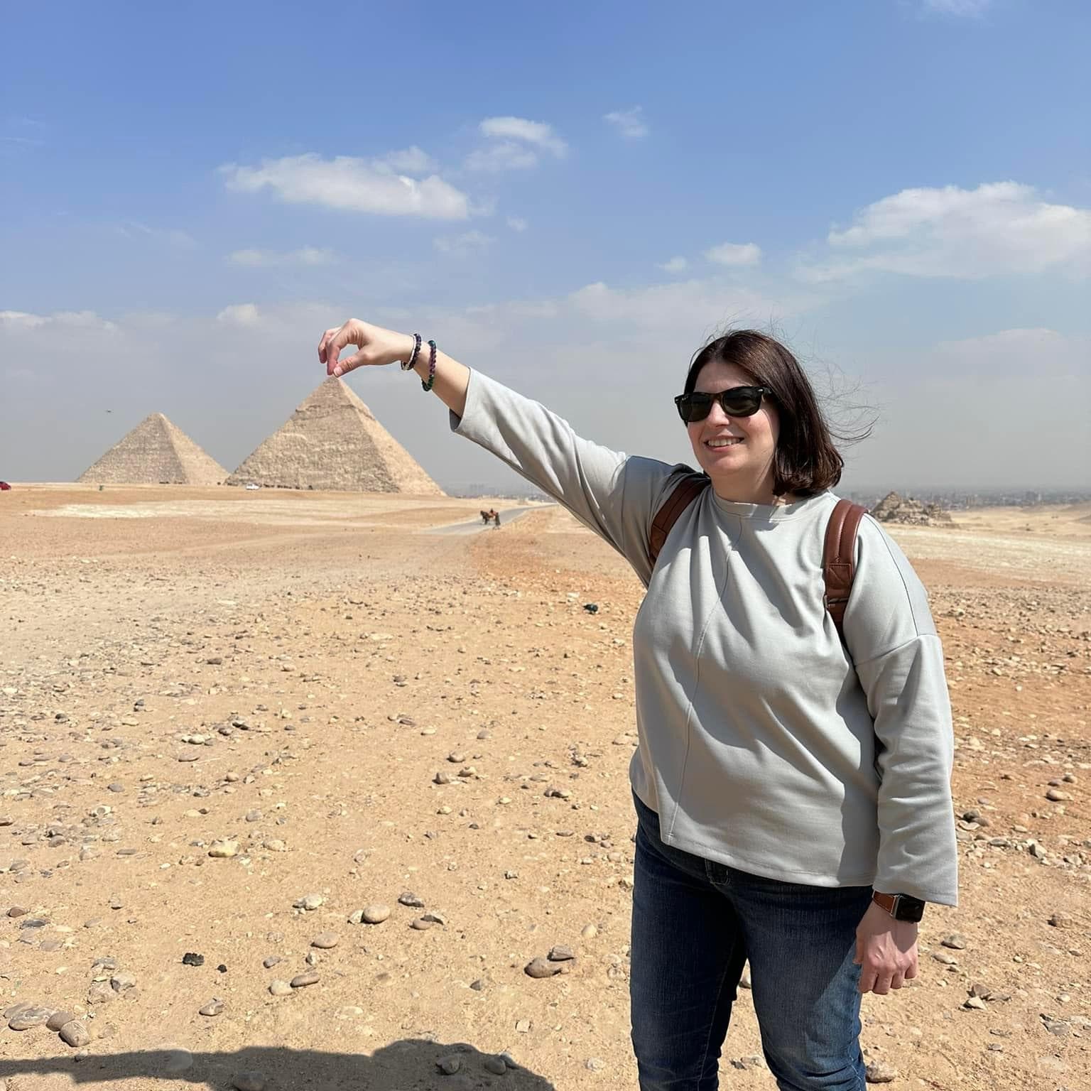 Tamara standing in front of the Great Pyramids in Egypt, with her hand positioned to look like she's holding the top of one