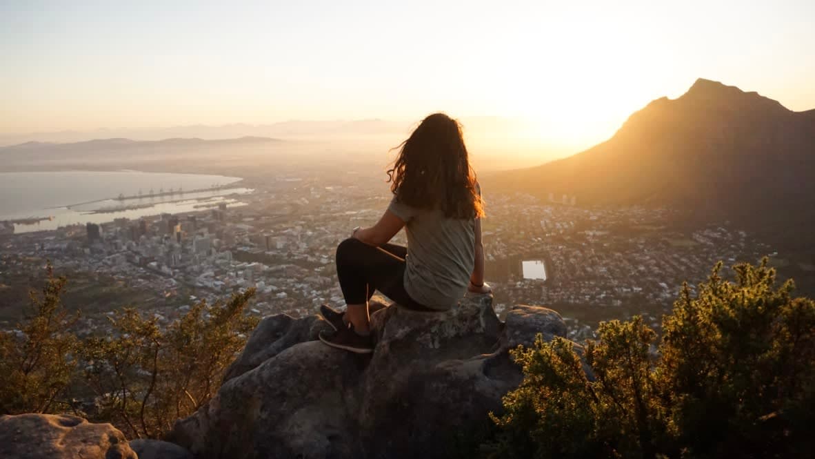 Aashima sitting on a rock at the mountain top looking at the view of the city, sea and mountains