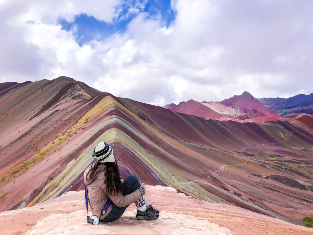 Aashima sitting on the ground and looking at the mesmerizing view of Vinicunca mountain