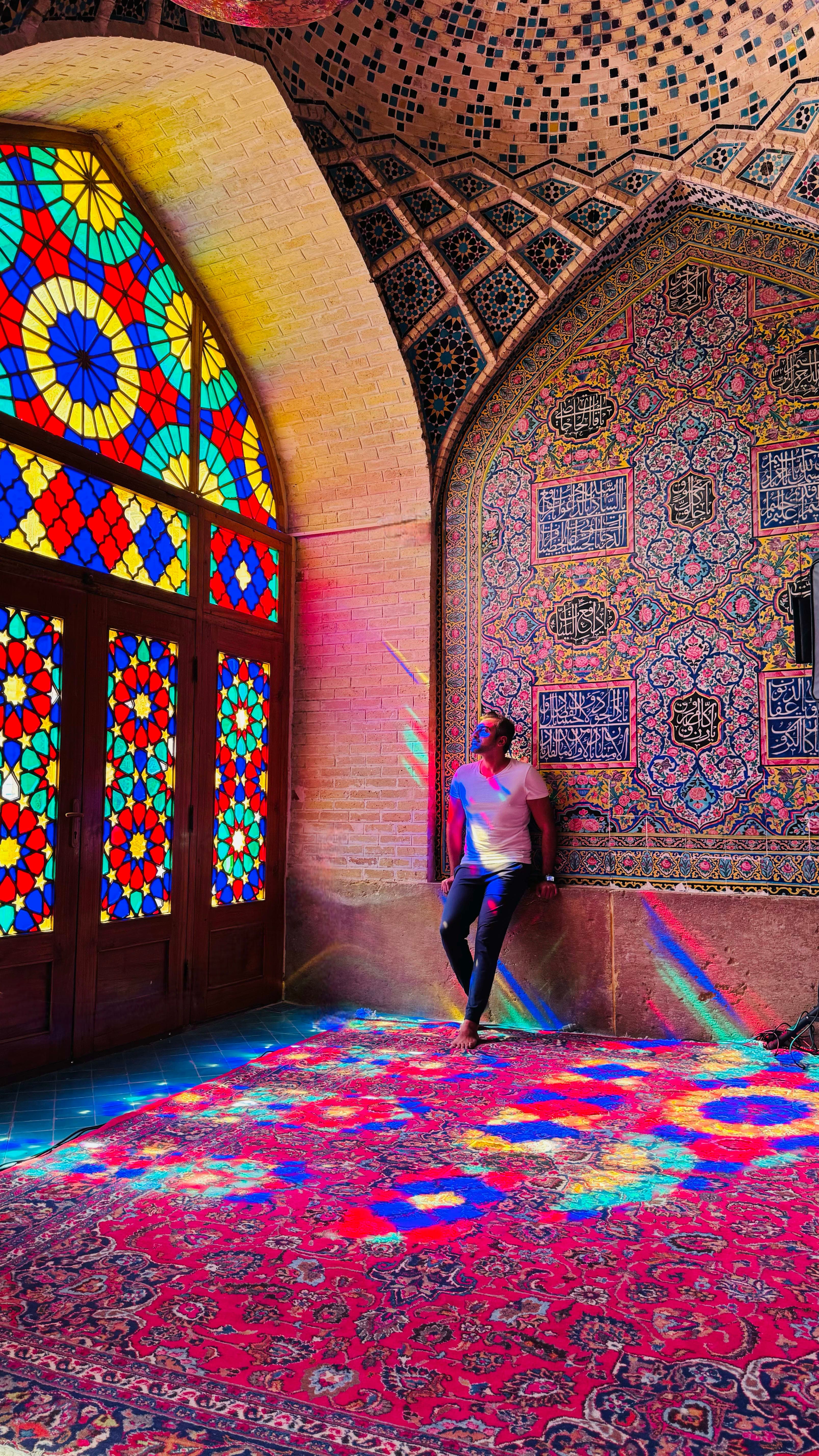 Advisor standing by a large colorful stained glass window with reflections of light on the ground of a mosque