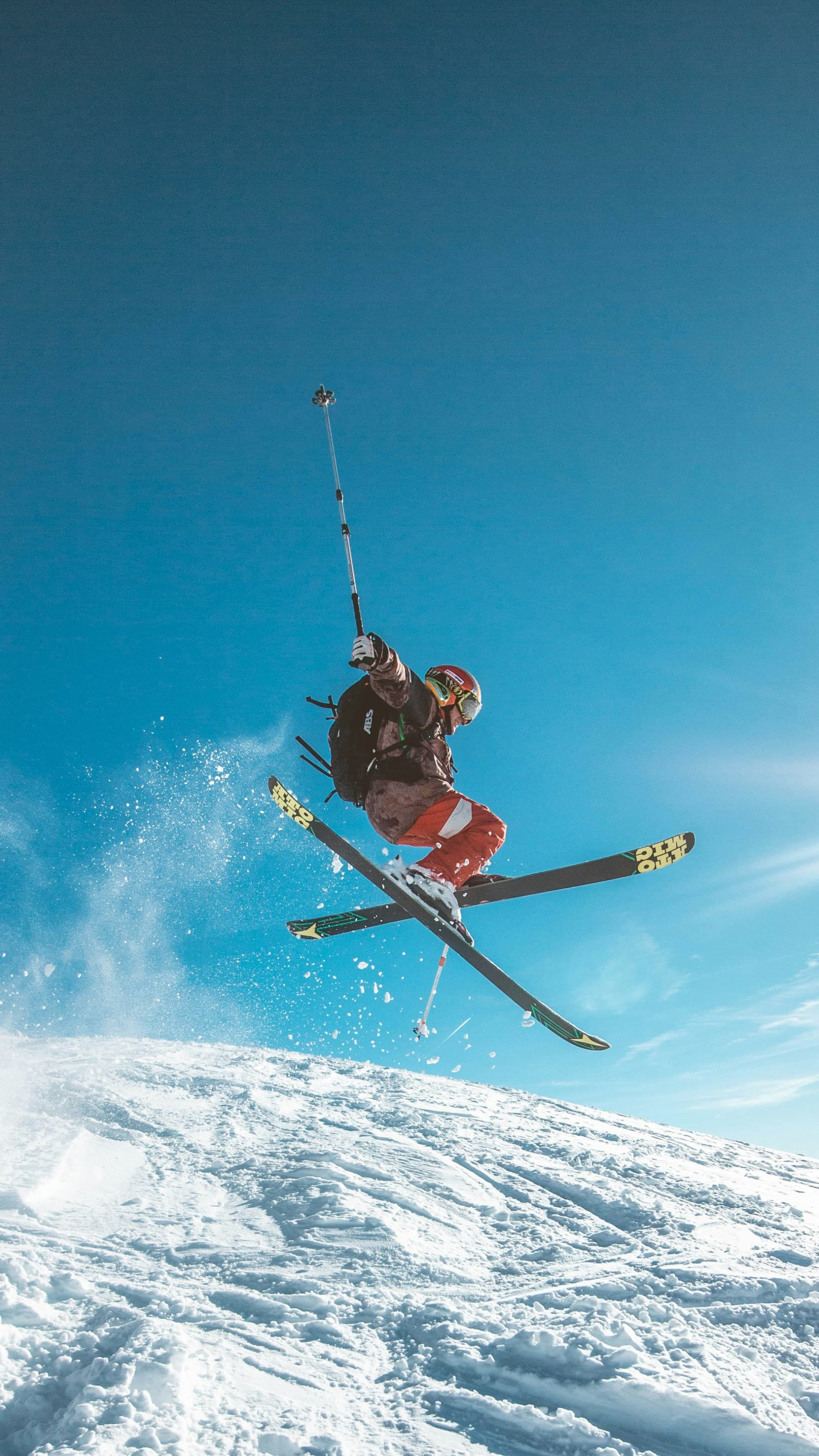 A man on skis jumps above the crest of a snowy hill with a clear blue sky behind.