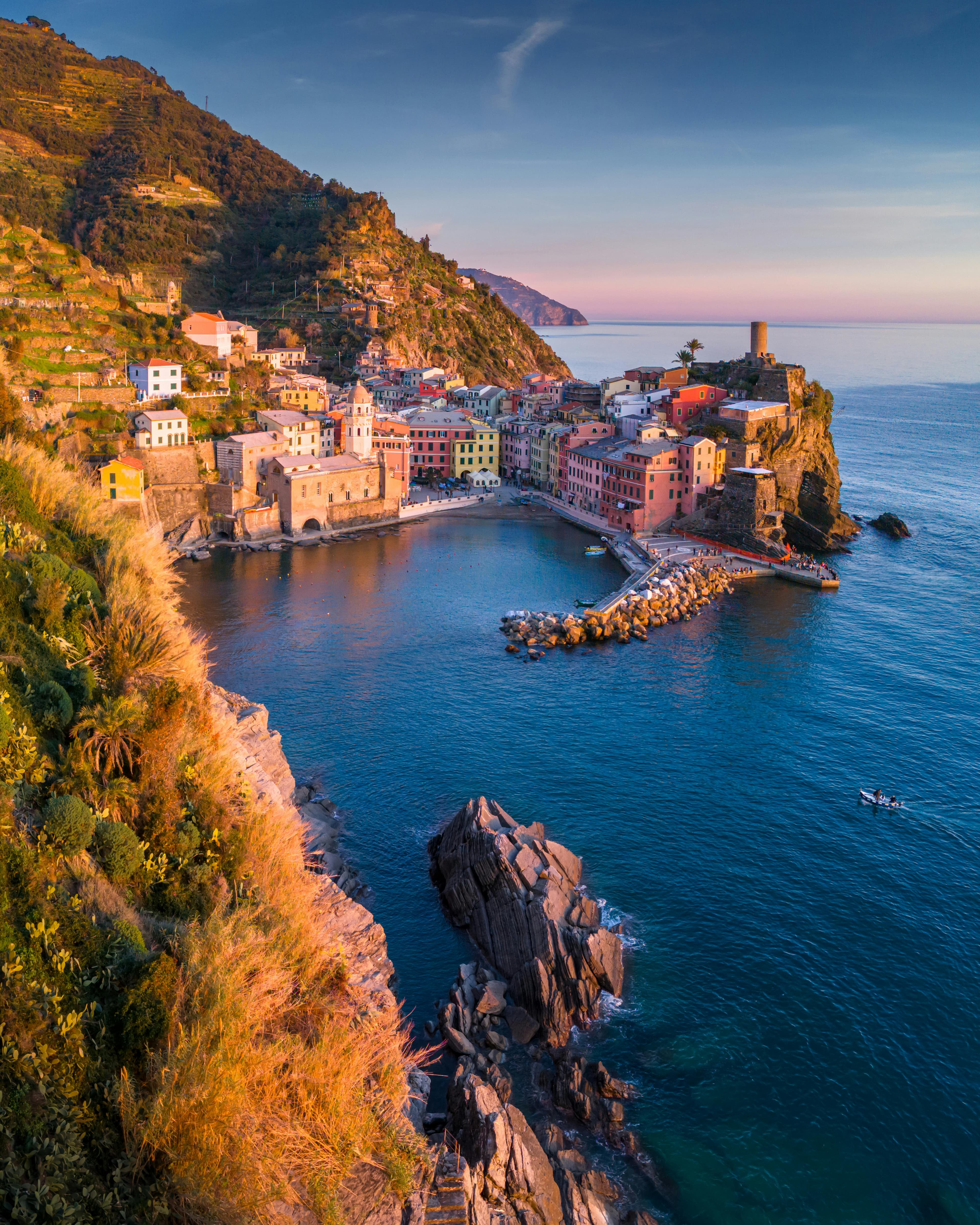 A view of a coastal town at sunset with rugged cliffs and calm water.