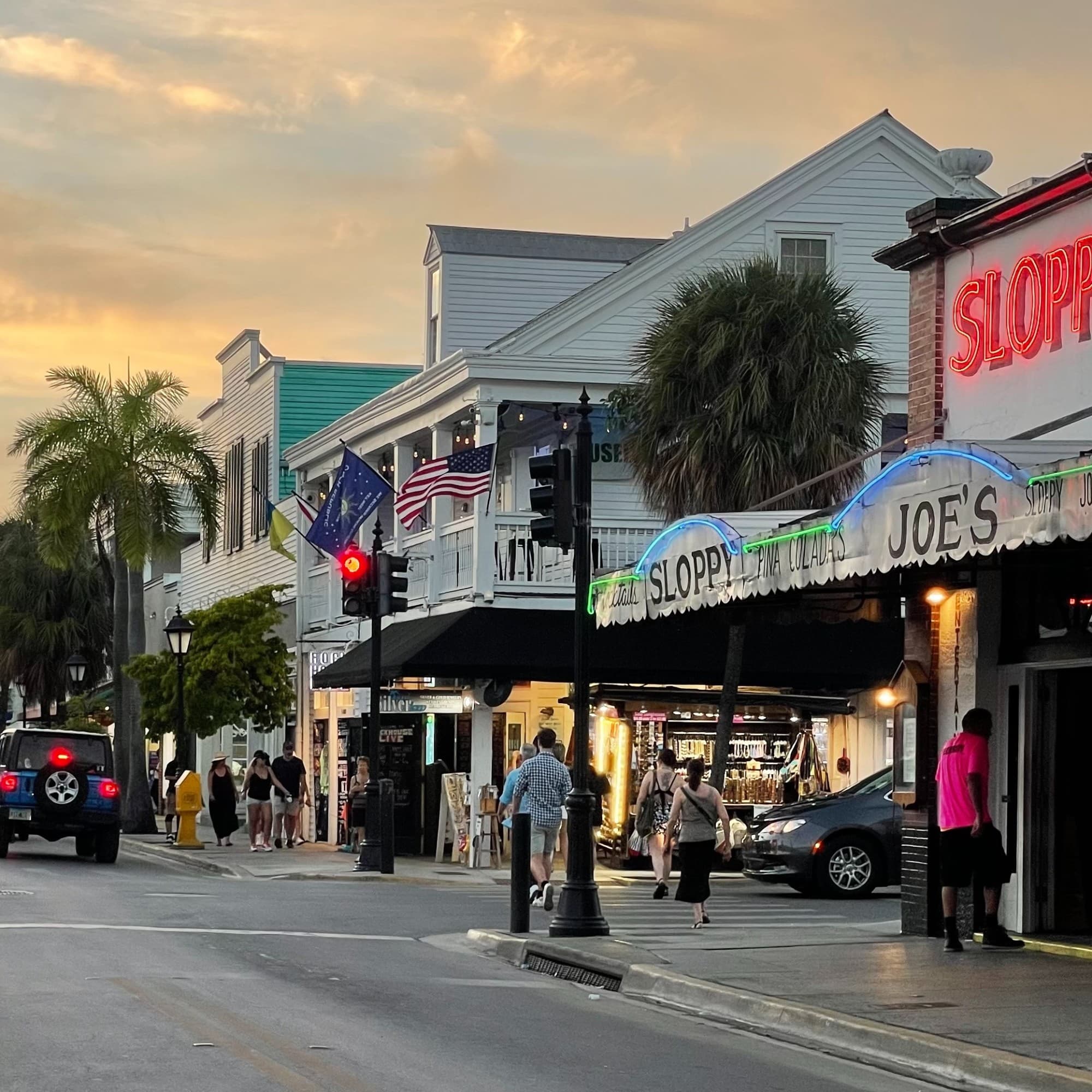 A bustling street scene at dusk with neon signs, American flags and pedestrians.
