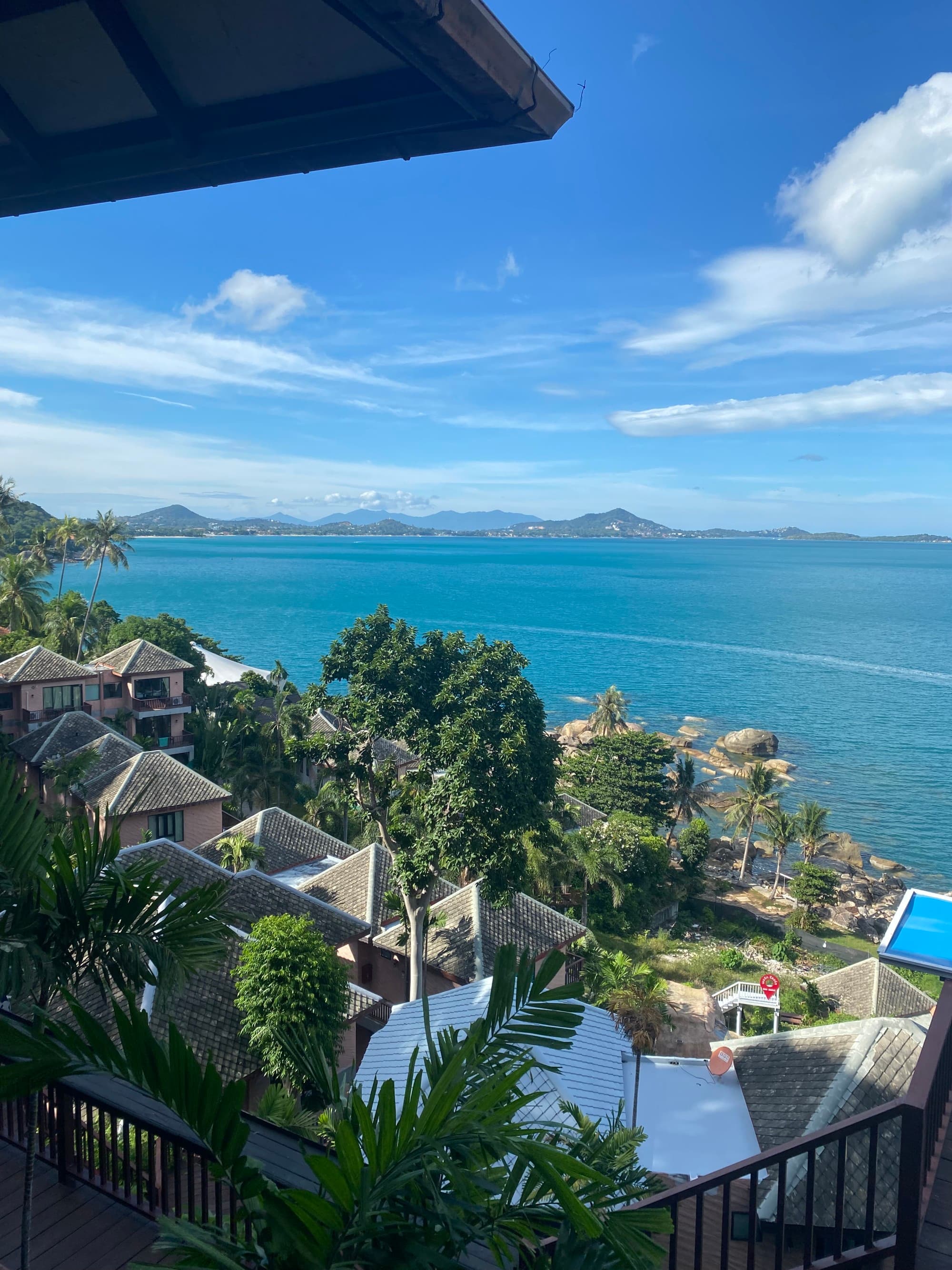 A serene coastal view with clear blue skies, tropical vegetation, and buildings overlooking the water.