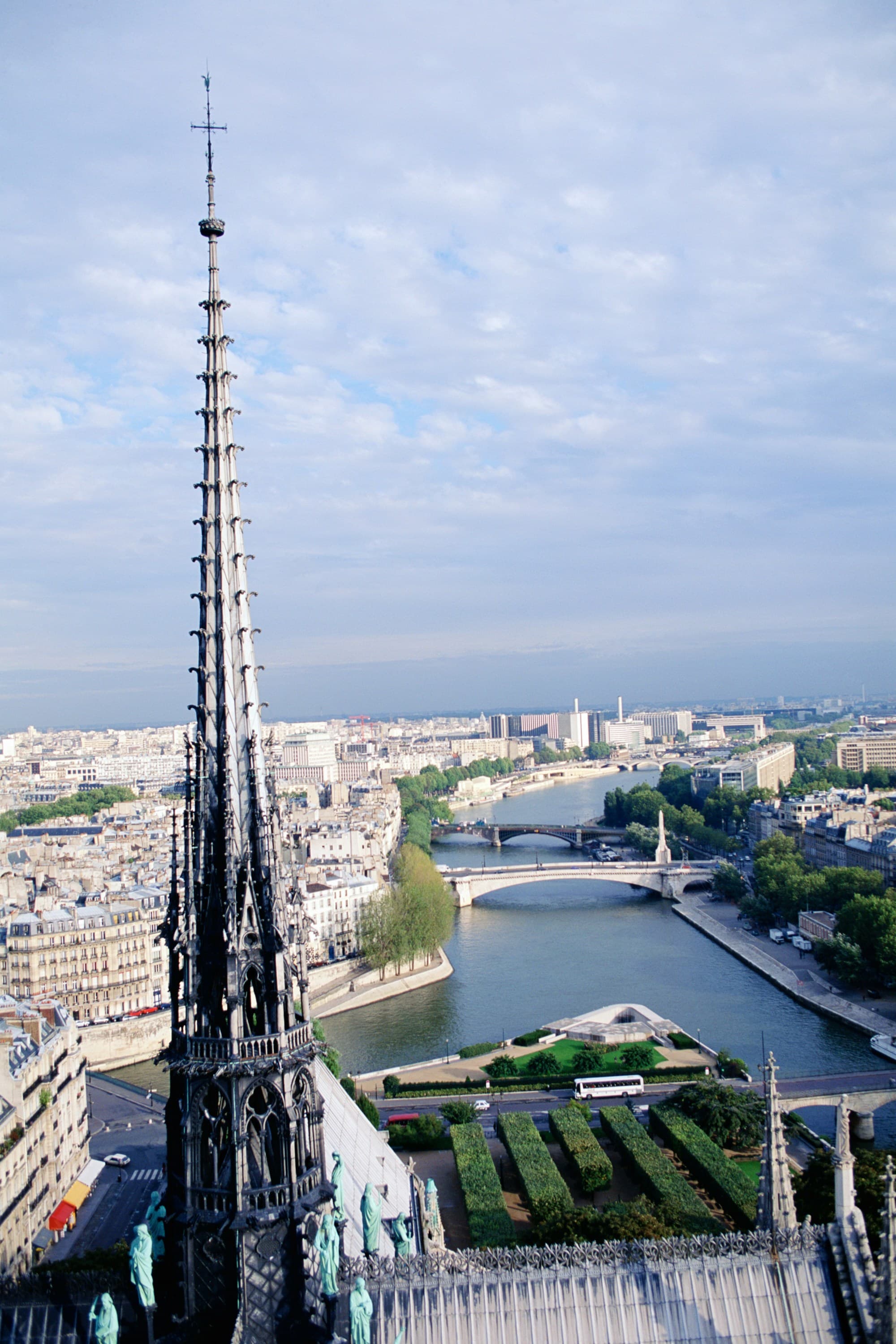 The image shows an aerial view of a cityscape with a prominent Gothic spire in the foreground and a river with bridges in the background.