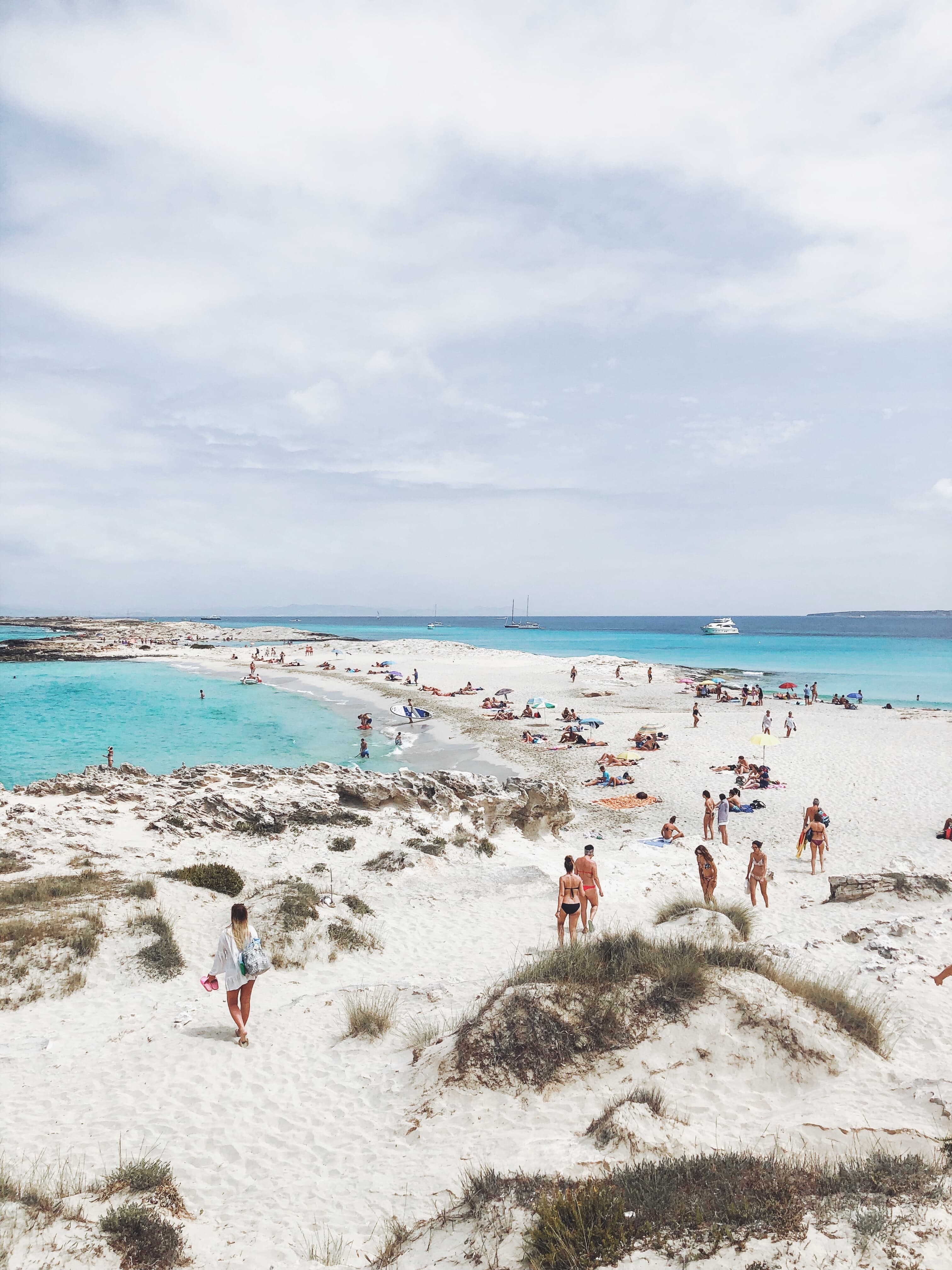 People walking on white sand beach next to blue water on a cloudy day