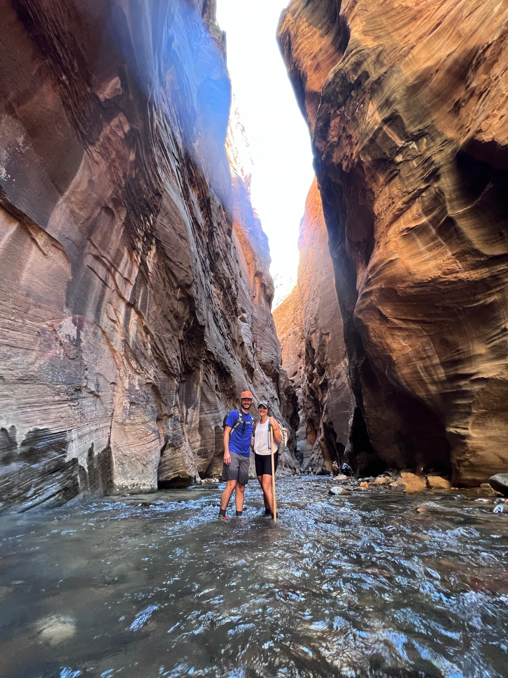 A man and woman standing in a river between rocky mountains.