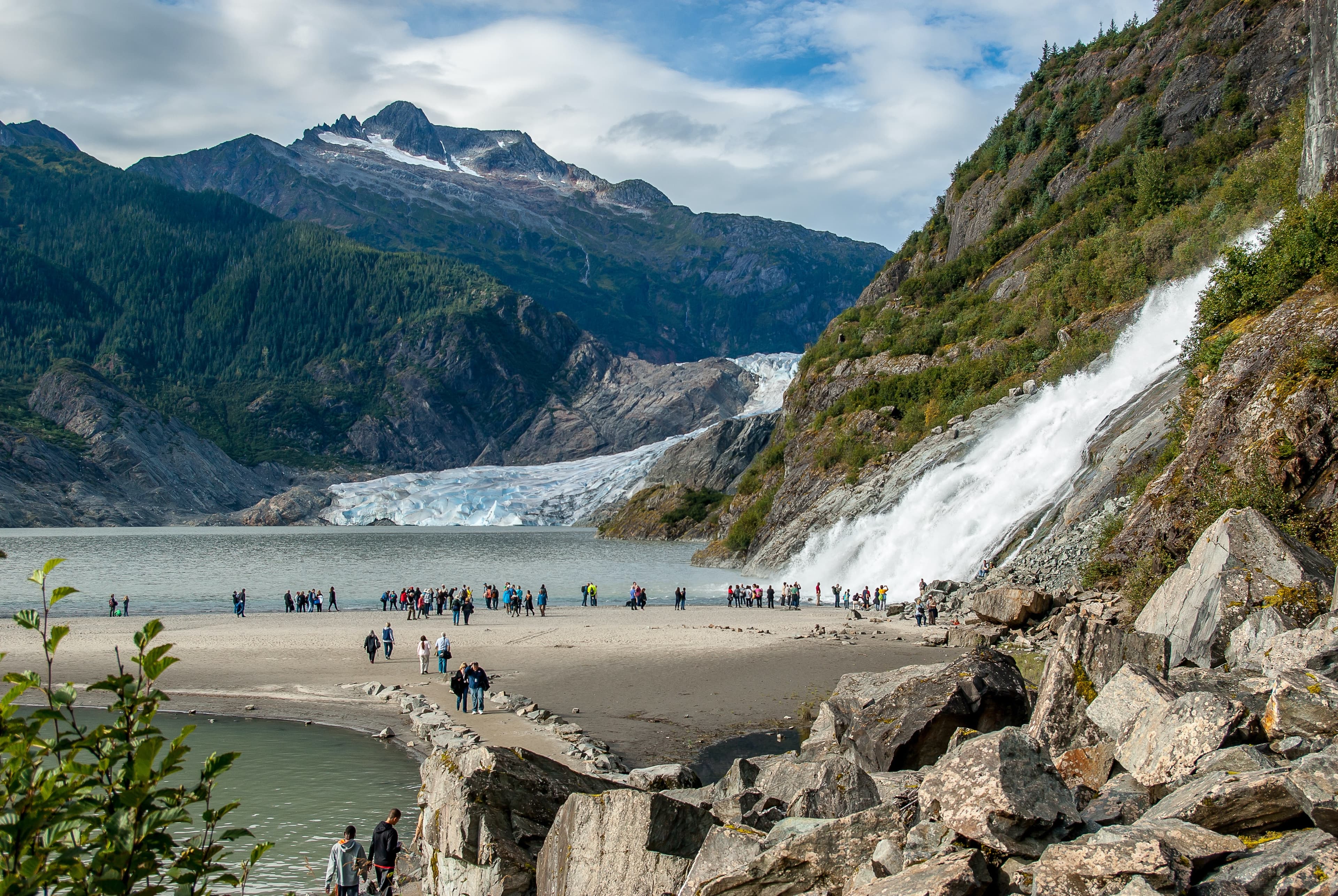 People standing next to body of water and mountains during daytime