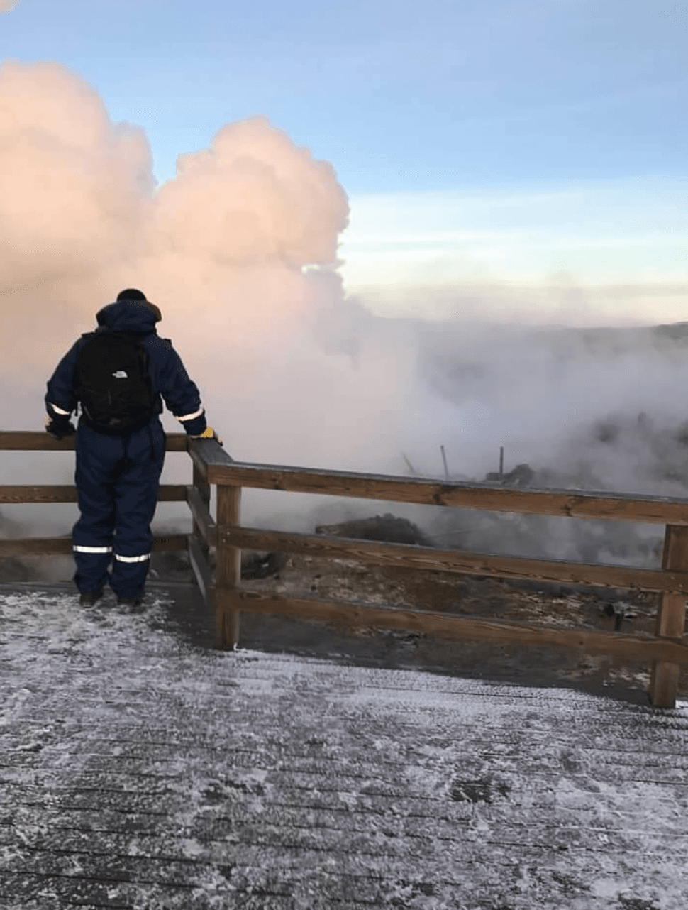 A person overlooking the smoke near a wooden fence outside.