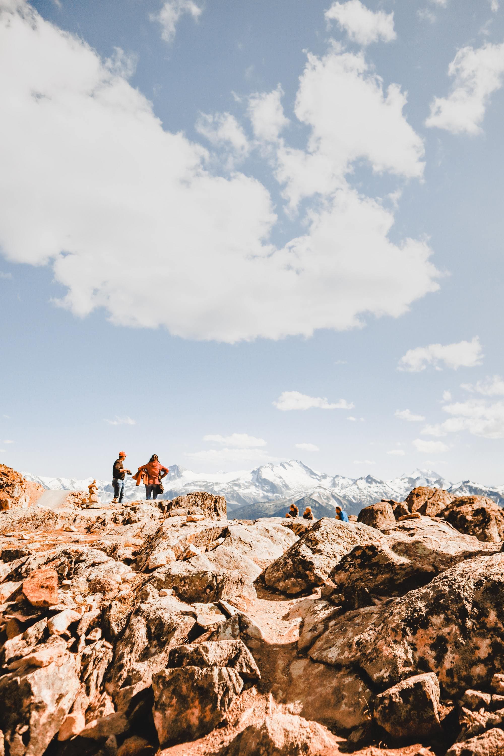 people stand on rock cliff at the peak of a mountain on a clear sunny day