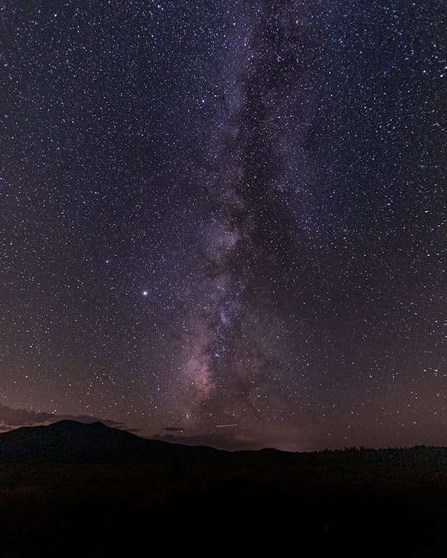 A view of a beautiful starry constellation at nighttime above a dark mountain top.
