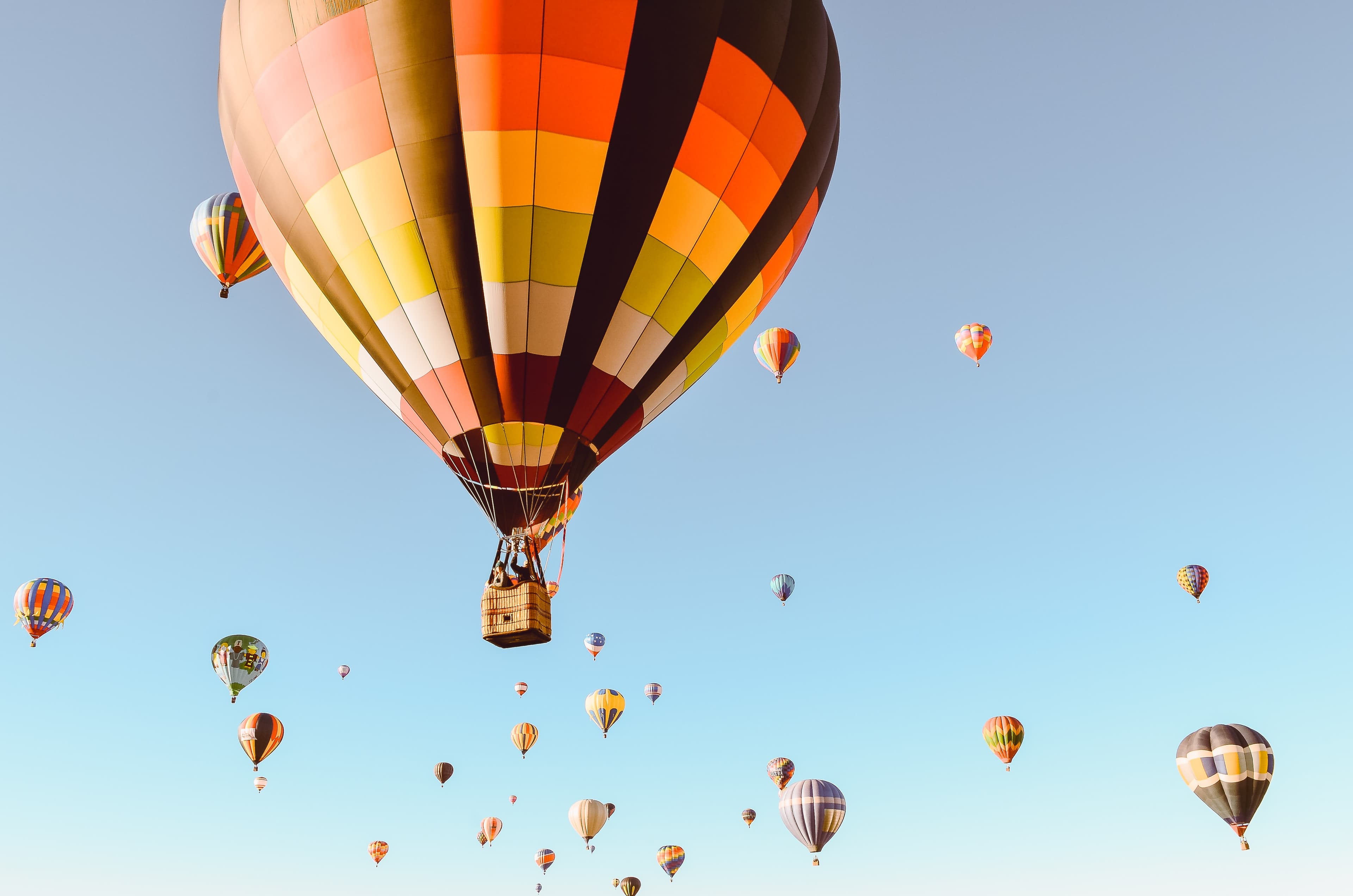 Red, yellow, white, orange, and black hot air balloon floats in the sky with other hot air balloons in the background in a clear blue sky