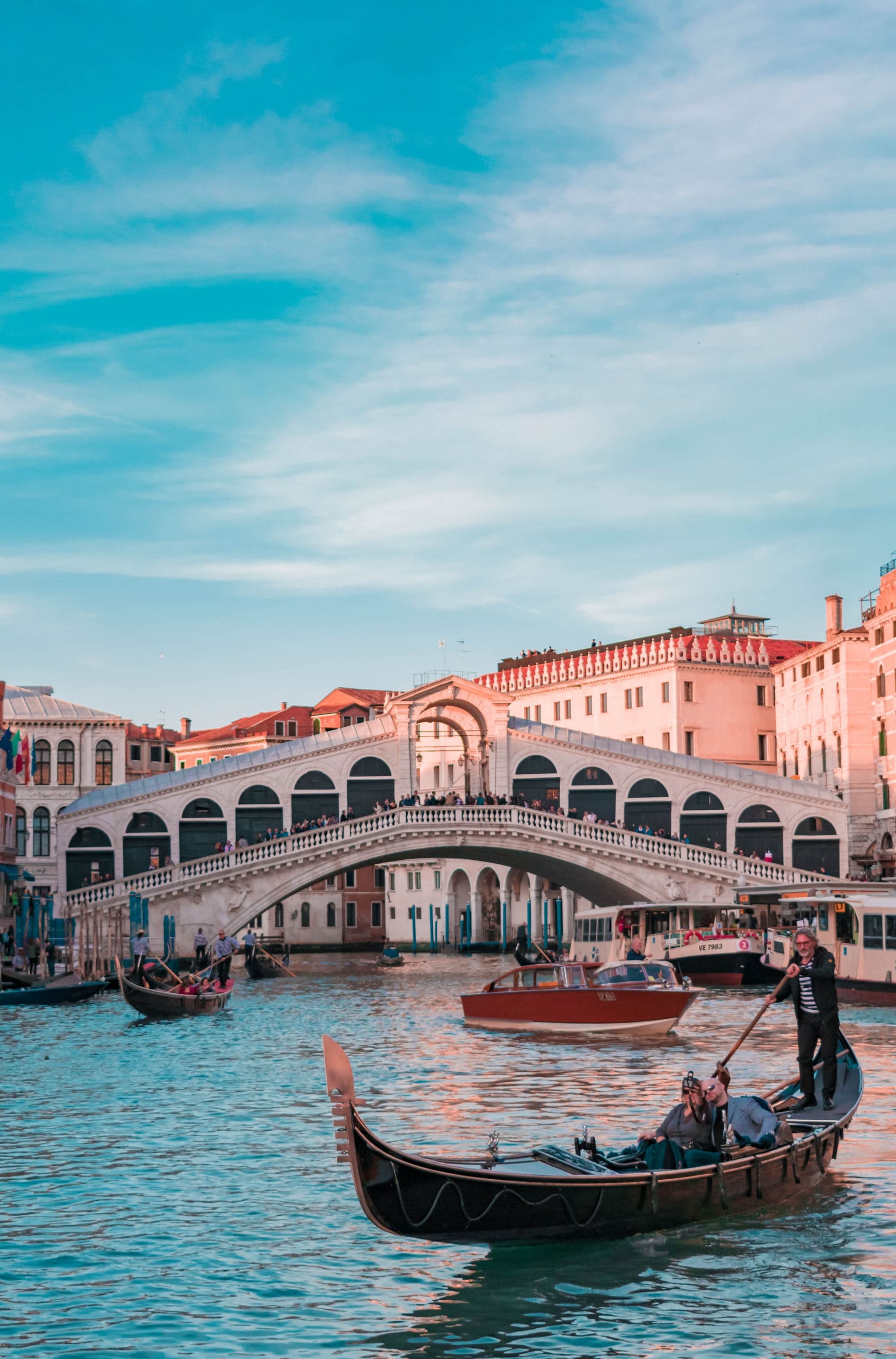 Man rowing a gondola boat on a canal beneath a bridge