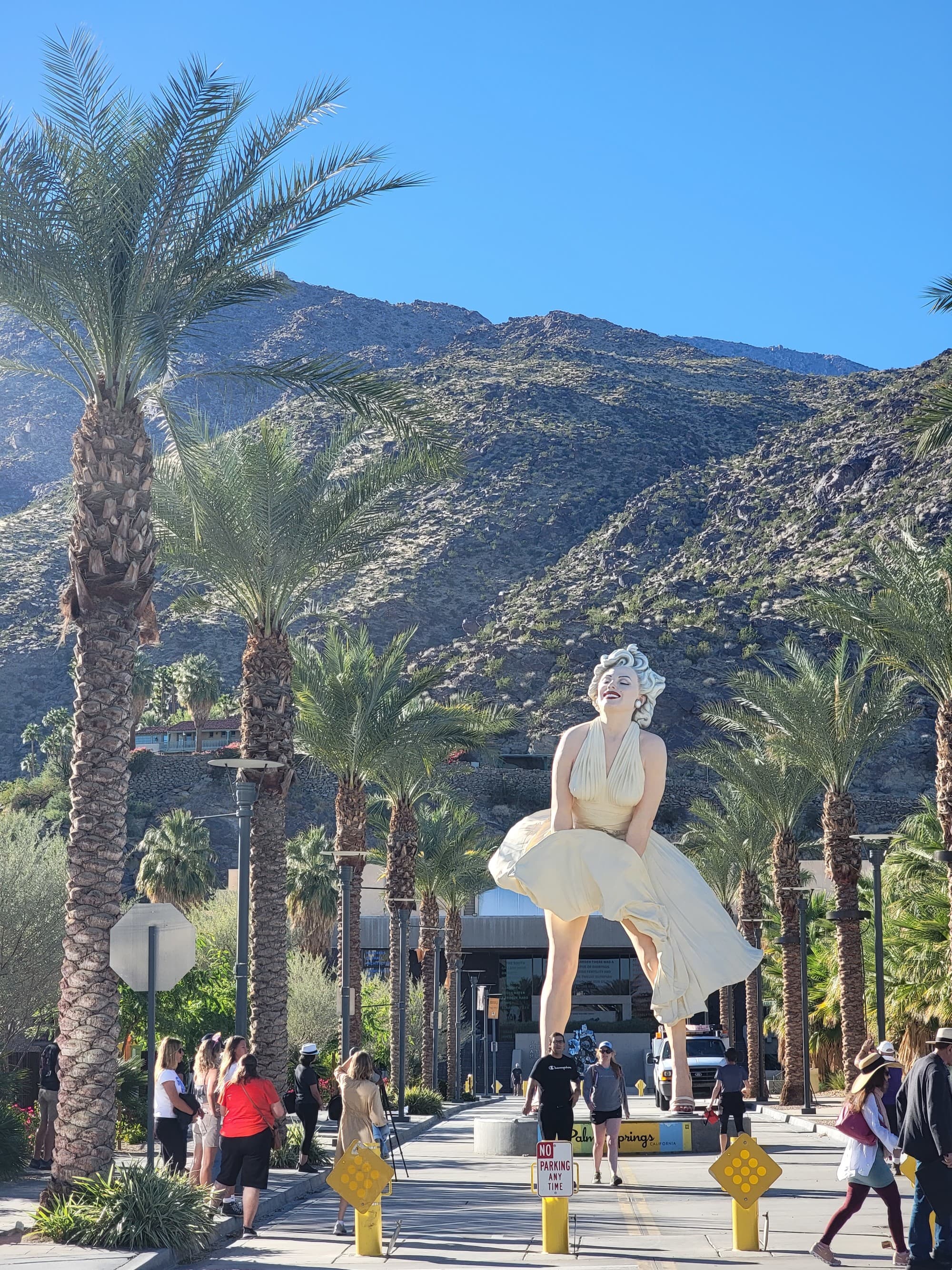 Statue of Marilyn Monroe between palm trees and in front of mountains.